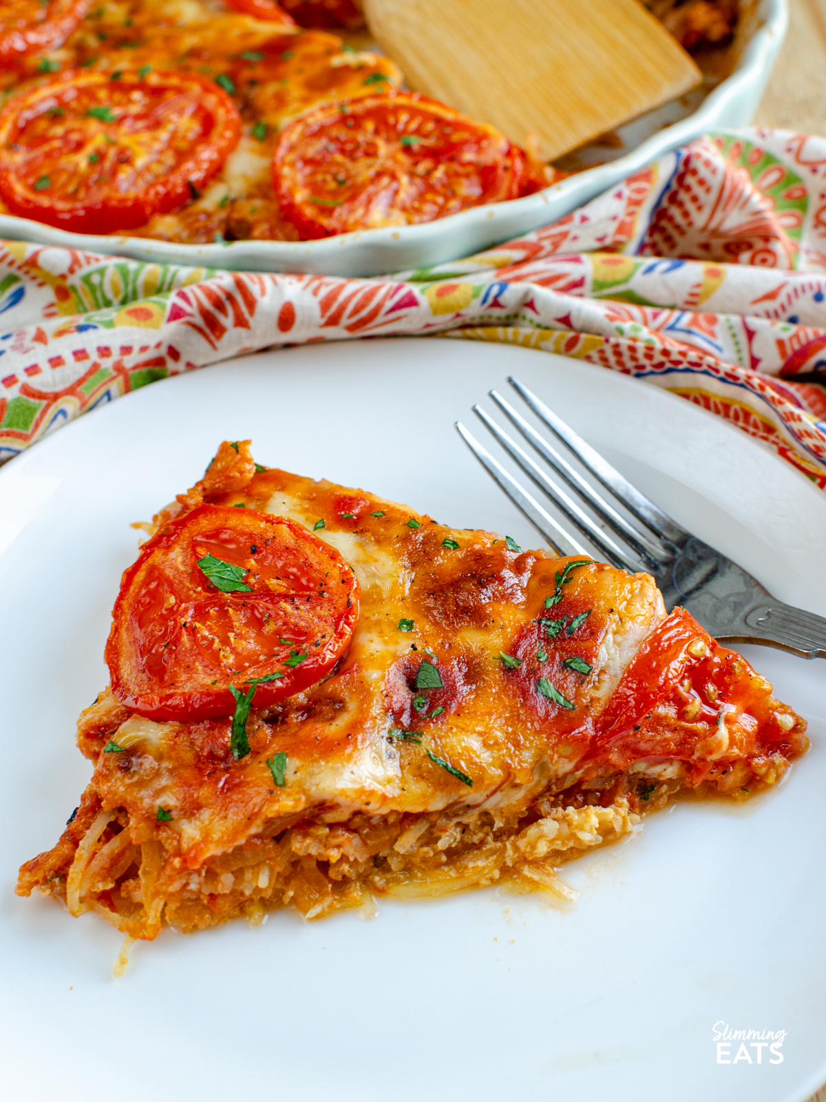 slice of cheesy tomato topped spaghetti squash bake on a white plate with a fork. 