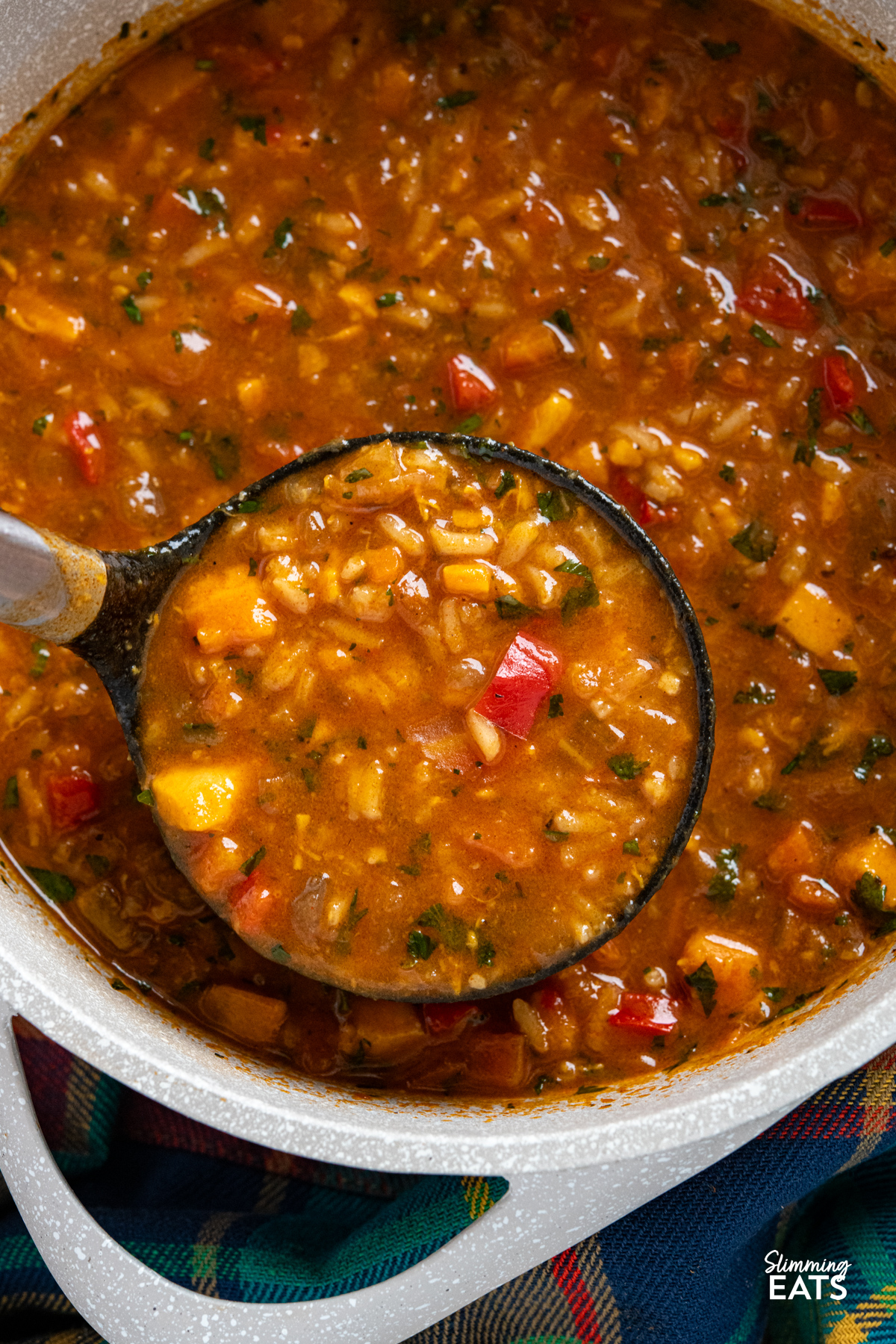 close up of beige double handled saucepan filled with Spicy Sweet Potato, Vegetable and Rice Soup with a ladle spooning some of the soup