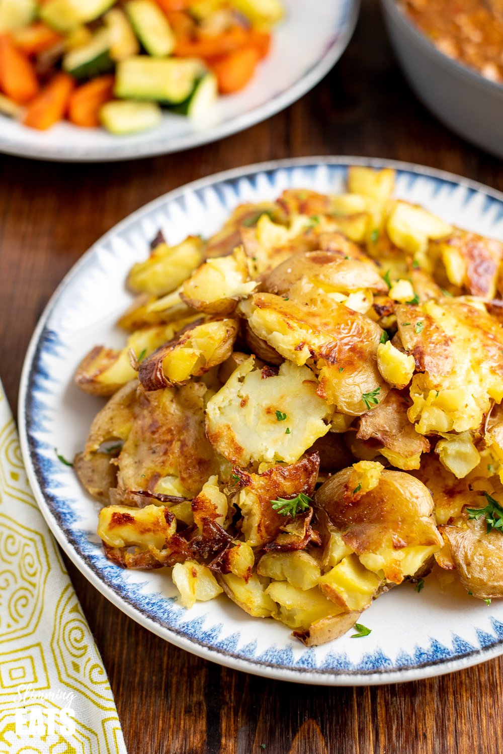 crushed roast potatoes on white plate with vegetables in background