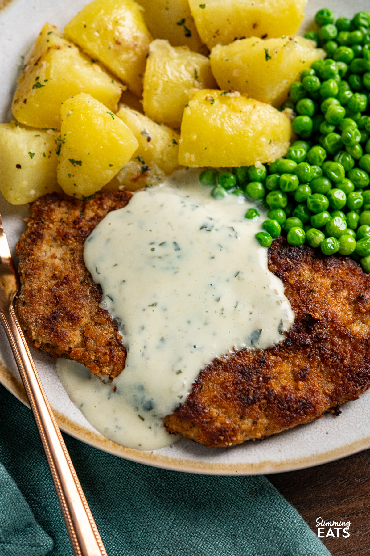 close up of Pork Schnitzel on plate drizzled with parsley sauce with lemon potatoes and garden peas