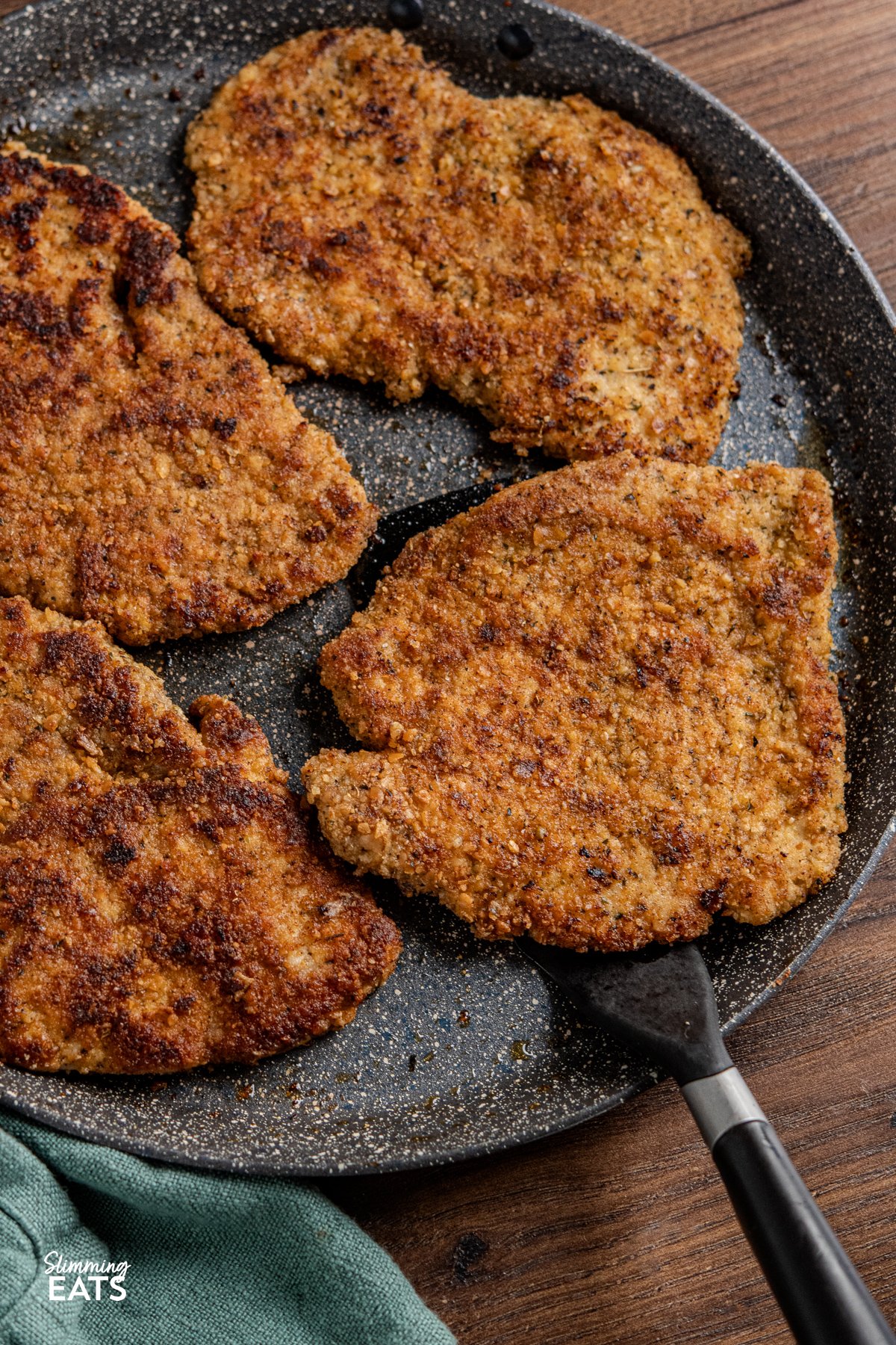 Indulge in a family-favourite pork schnitzel, featuring tender cutlets coated in seasoned wholemeal breadcrumbs, pan-fried to golden perfection, and served with a delicious creamy parsley sauce. Golden breaded pork schnitzel on a non stick ceramic pan