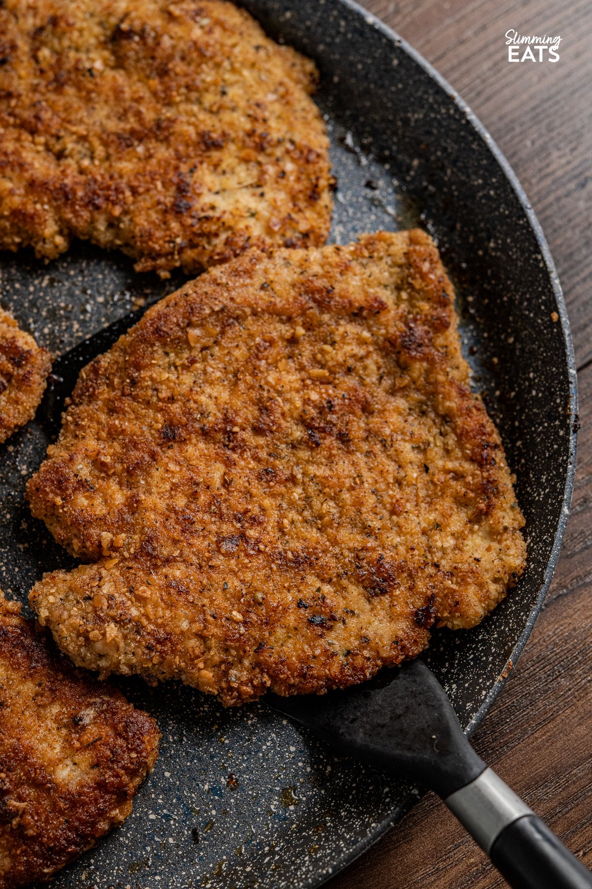 Indulge in a family-favourite pork schnitzel, featuring tender cutlets coated in seasoned wholemeal breadcrumbs, pan-fried to golden perfection, and served with a delicious creamy parsley sauce. close up of Golden breaded pork schnitzel on a non stick ceramic pan