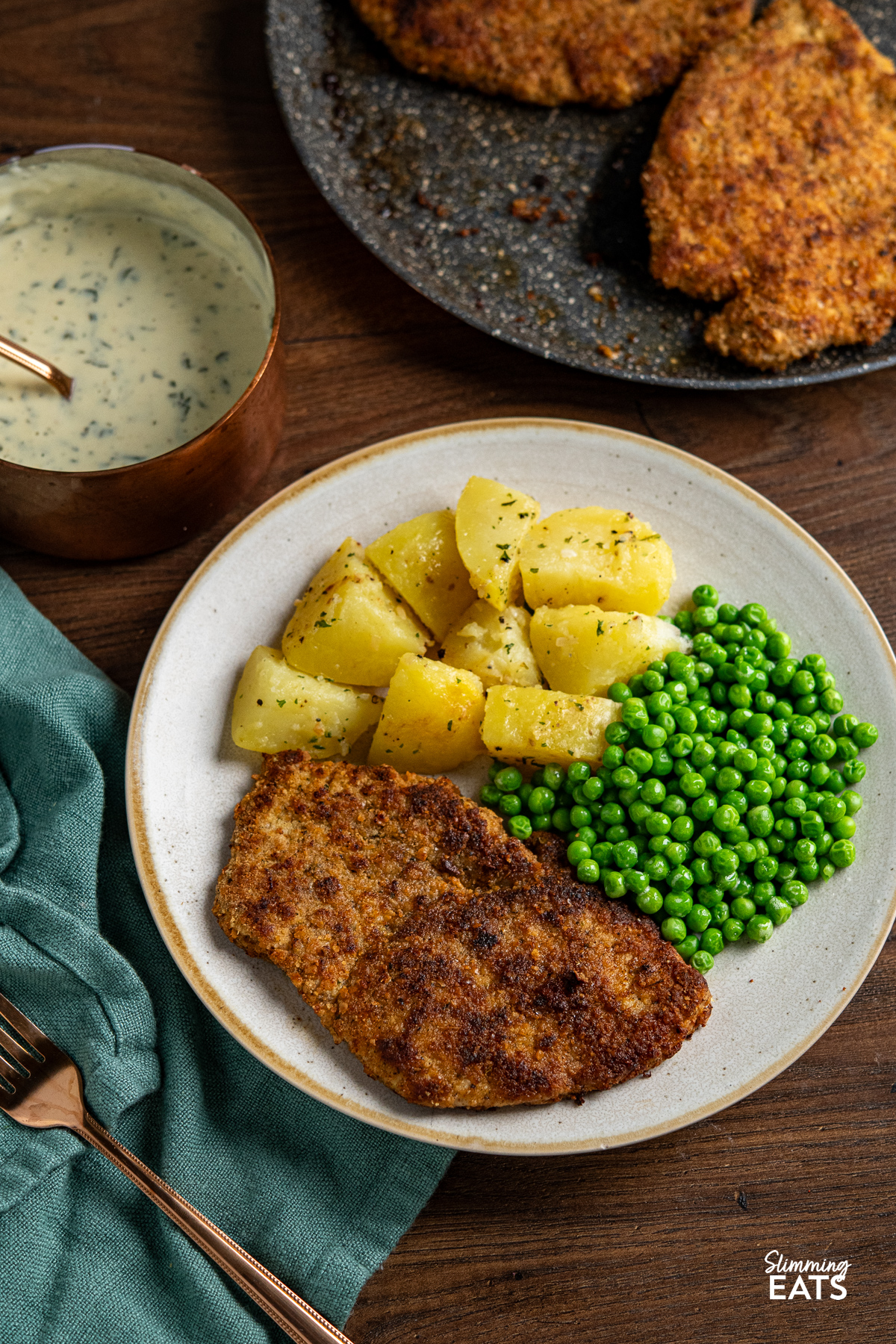 Pork Schnitzel on plate with lemon potatoes and garden peas, small sauce of parsley sauce in background