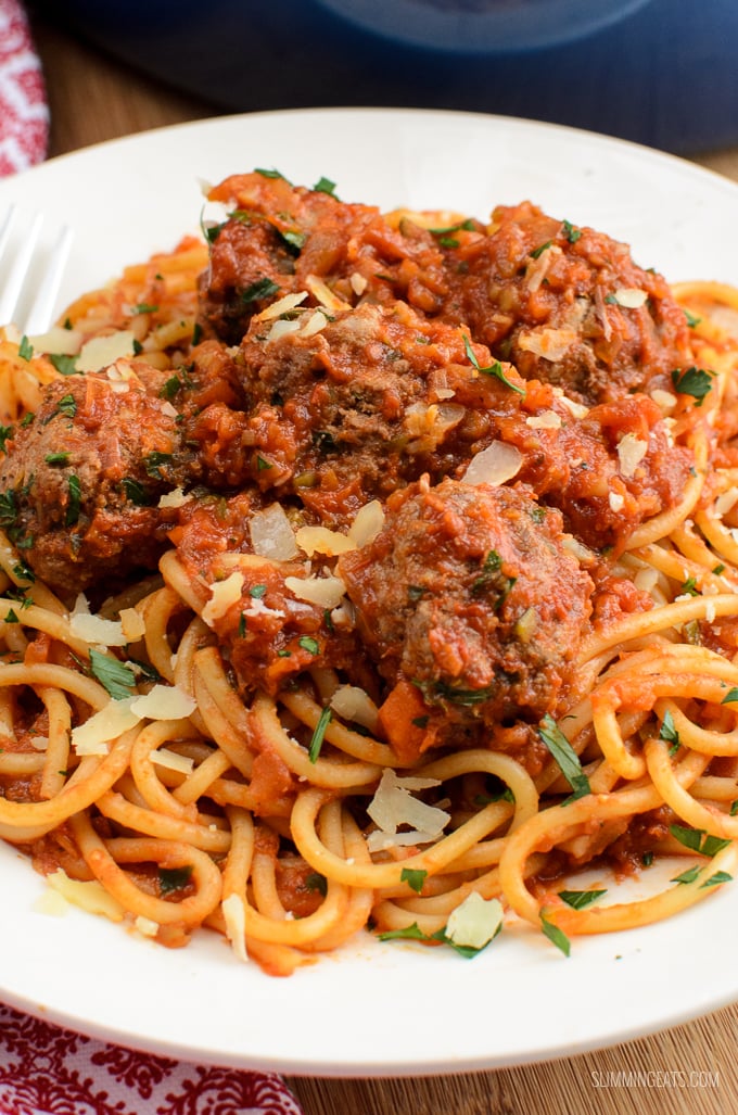 close up of spaghetti and meatballs served on a white plate sprinkled with grated parmesan