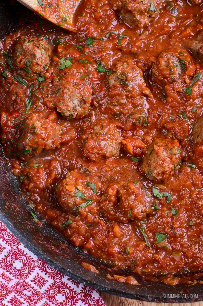 Tender homemade beef meatballs in a rich tomato sauce, served with spaghetti, make for the perfect family meal. meatballs in tomato veggies sauce in a frying pan with wooden spoon