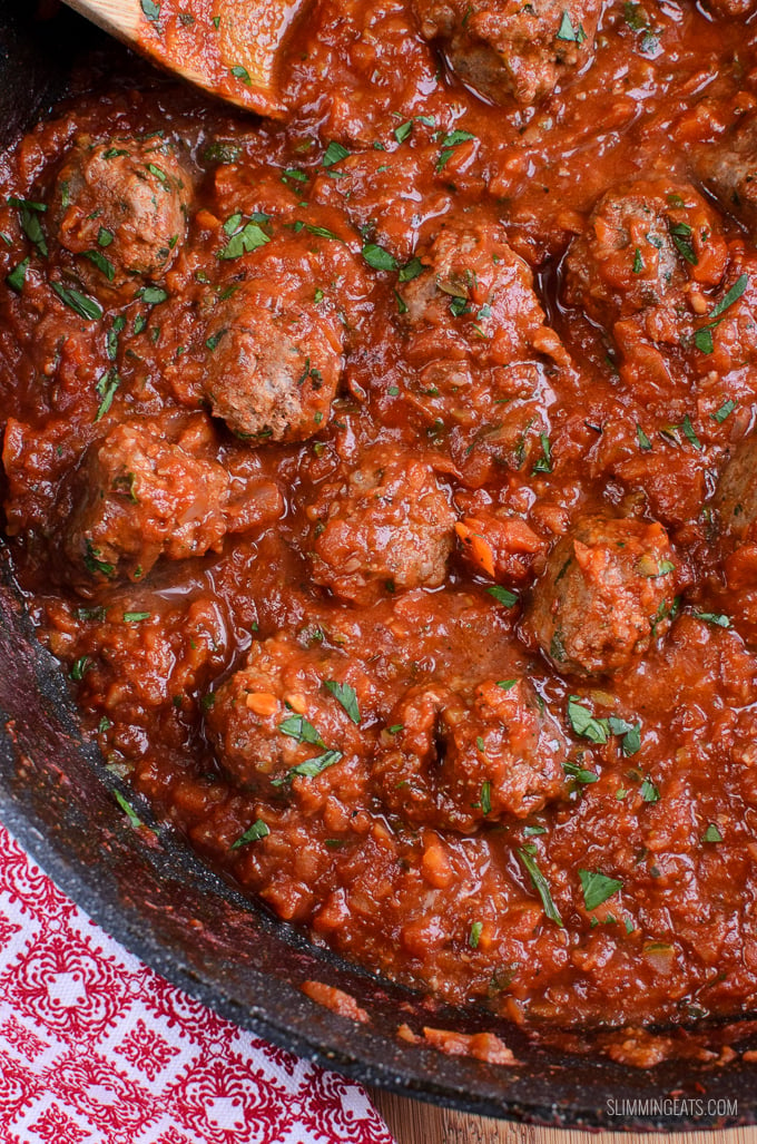 meatballs in tomato veggies sauce in a frying pan with wooden spoon