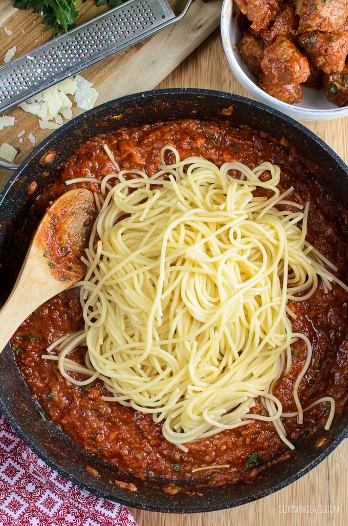 Tender homemade beef meatballs in a rich tomato sauce, served with spaghetti, make for the perfect family meal. spaghetti piled on top of meatballs in tomato veggies sauce in a frying pan with wooden spoon