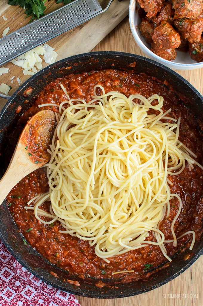 spaghetti piled on top of meatballs in tomato veggies sauce in a frying pan with wooden spoon