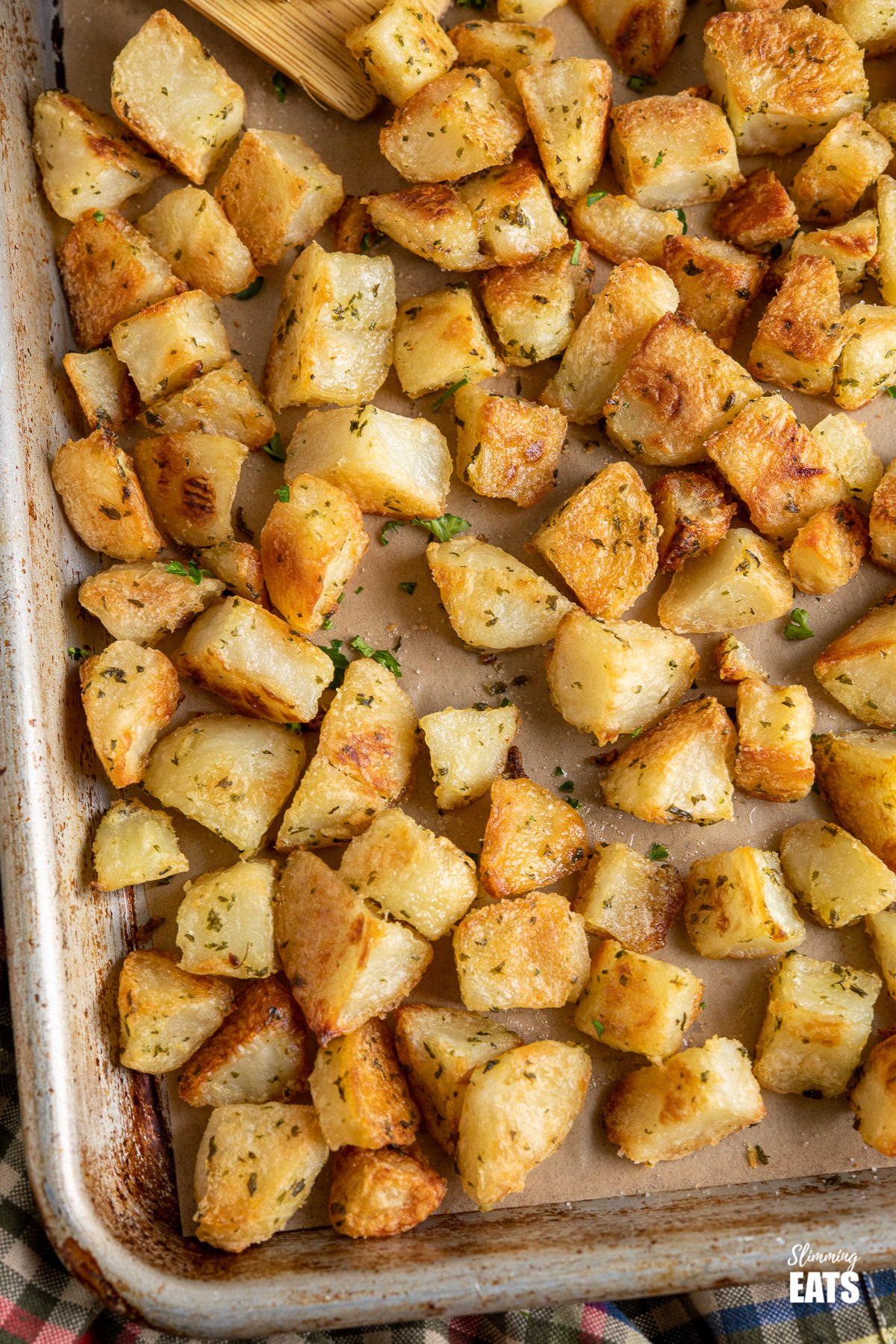 Garlic and Herb Roasted Potatoes (from www.slimmingeats.com) - crispy on the outside, fluffy on the inside with the delicious flavours of garlic and herbs make these the perfect side for a variety of main meals. #glutenfree #dairyfree #vegan #vegetarian #slimmingworld #weightwatchers close up of Garlic and Herb Roasted Potatoes on baking tray
