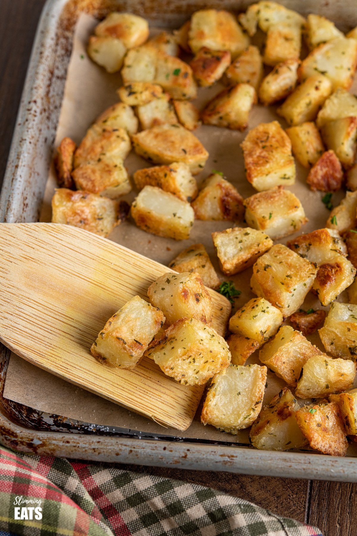 Garlic and Herb Roasted Potatoes (from www.slimmingeats.com) - crispy on the outside, fluffy on the inside with the delicious flavours of garlic and herbs make these the perfect side for a variety of main meals. #glutenfree #dairyfree #vegan #vegetarian #slimmingworld #weightwatchers close up of Garlic and Herb Roasted Potatoes on a wooden spatula from baking tray