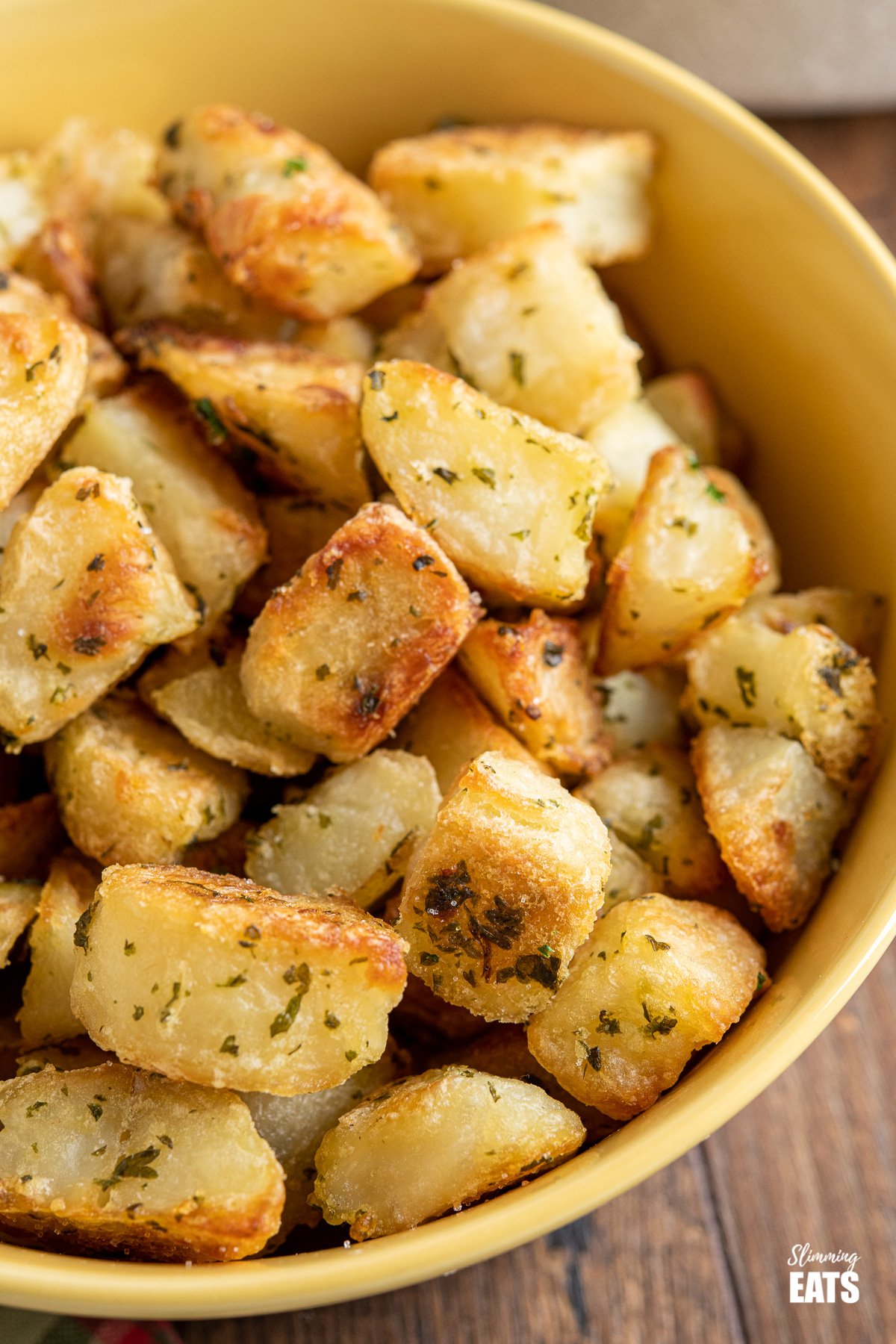 Garlic and Herb Roasted Potatoes (from www.slimmingeats.com) - crispy on the outside, fluffy on the inside with the delicious flavours of garlic and herbs make these the perfect side for a variety of main meals. #glutenfree #dairyfree #vegan #vegetarian #slimmingworld #weightwatchers close up of Garlic and Herb Roasted Potatoes in a yellow bowl