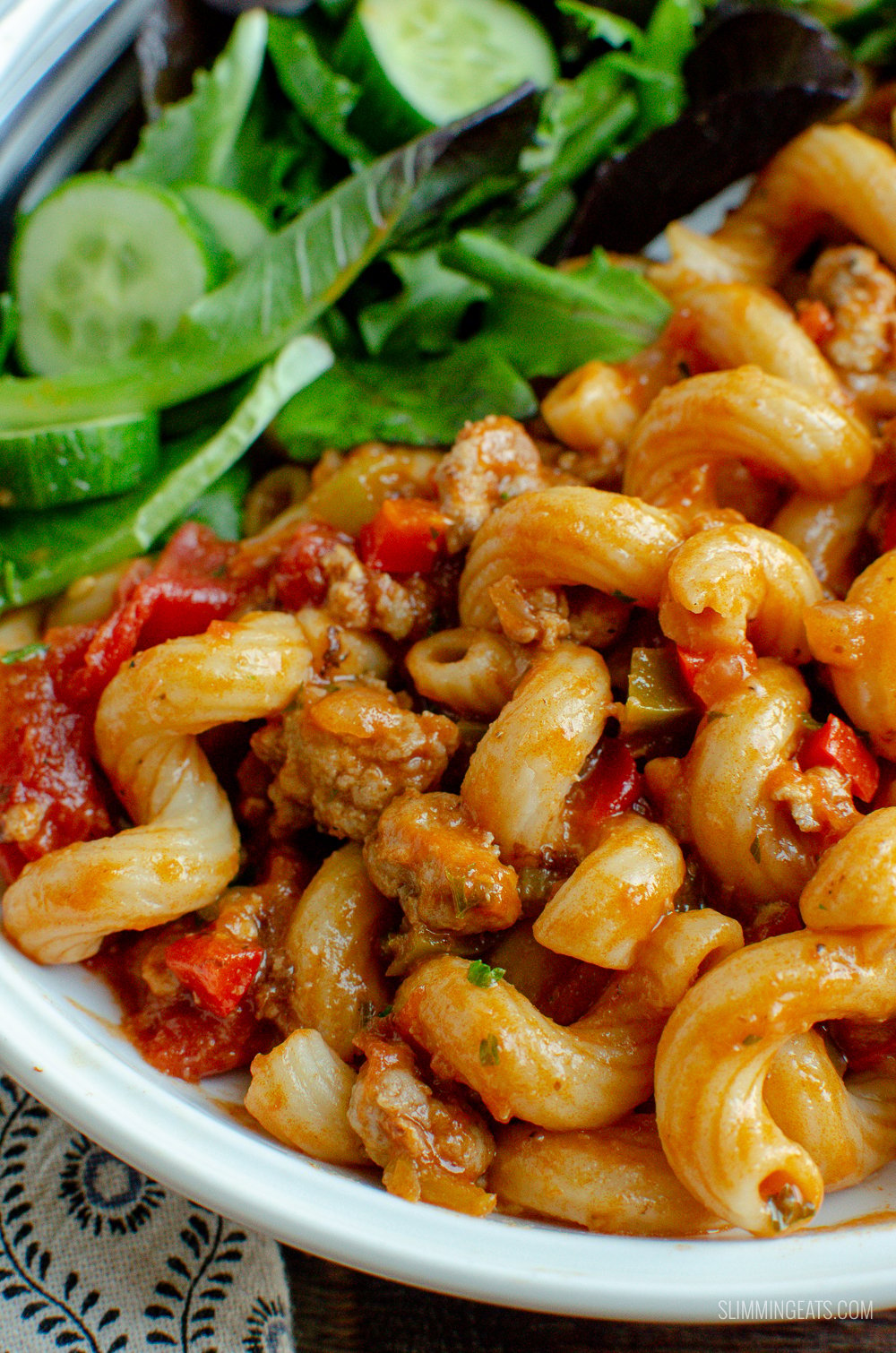 close up of sausage and tomato pasta in white bowl with salad
