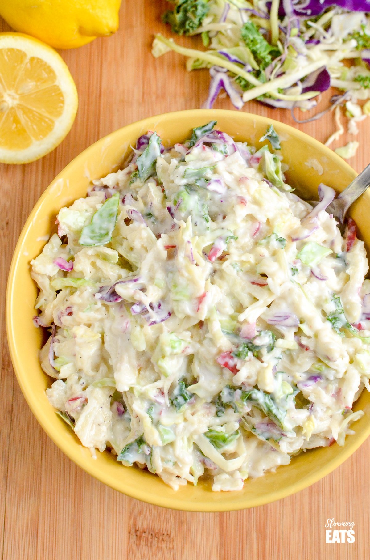 Sweet Tangy and Creamy Apple Coleslaw in a yellow bowl with scattered halved lemons.