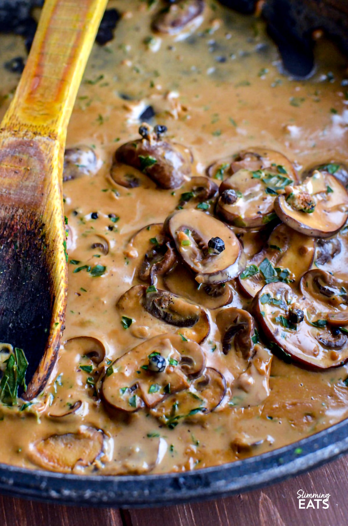 Creamy peppercorn mushroom sauce simmering in a frying pan, stirred with a wooden spoon.