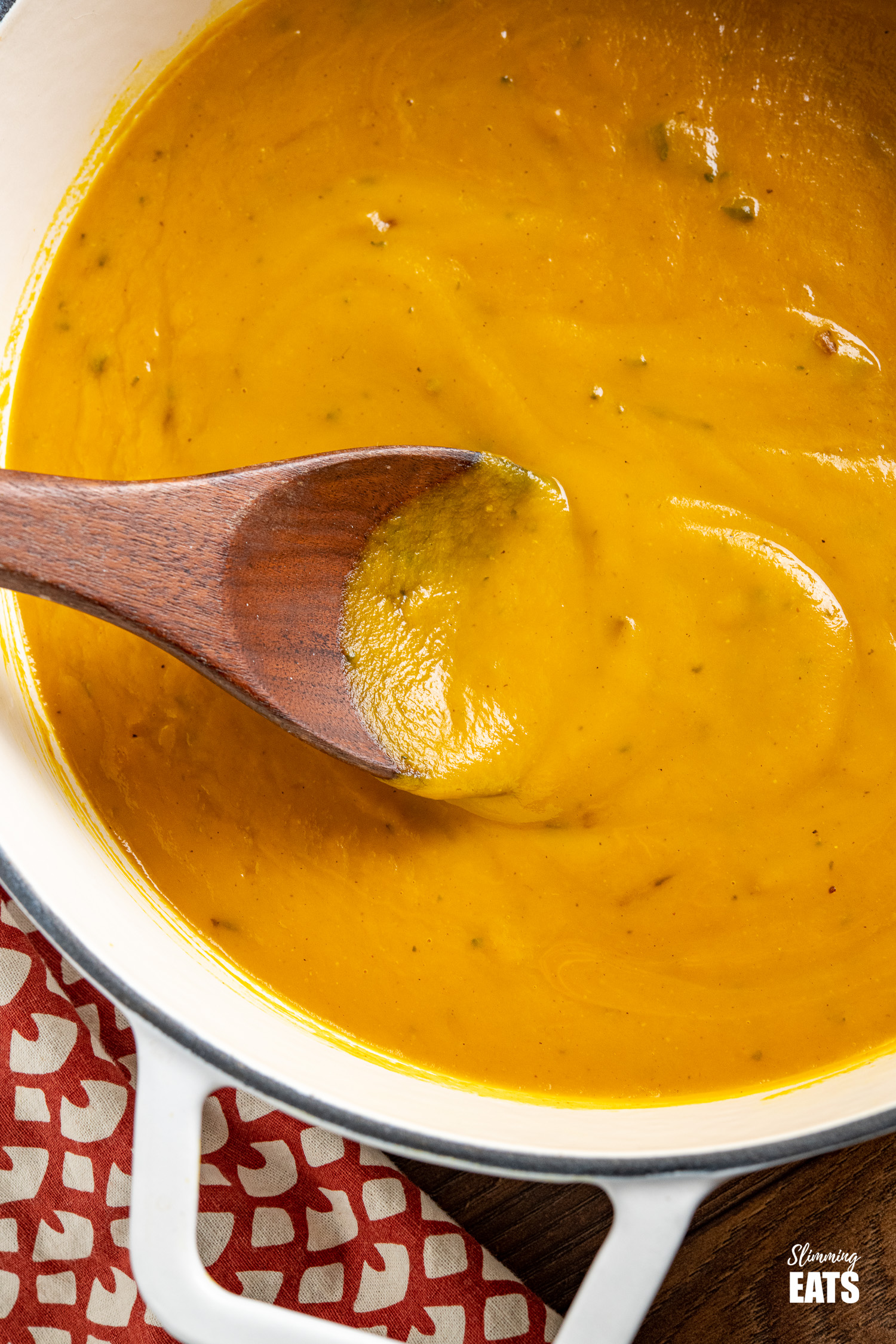 close up of butternut squash soup in white cast iron pot with dark wooden spoon