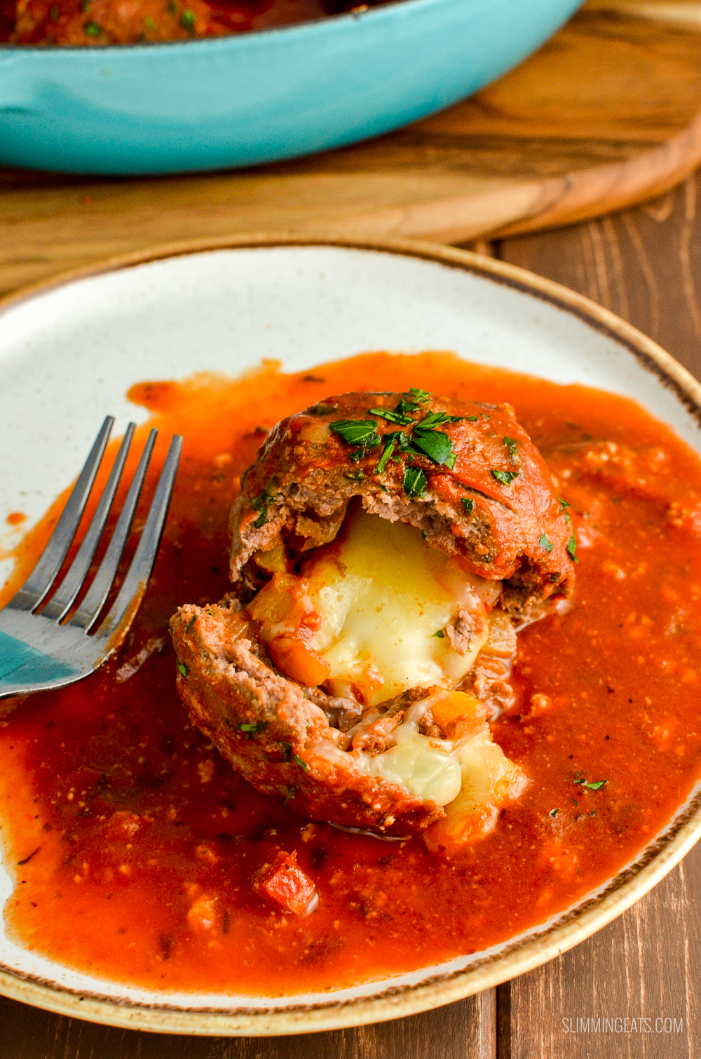 broken open mega stuffed meatball with oozy melted mozzarella on place with tomato sauce
