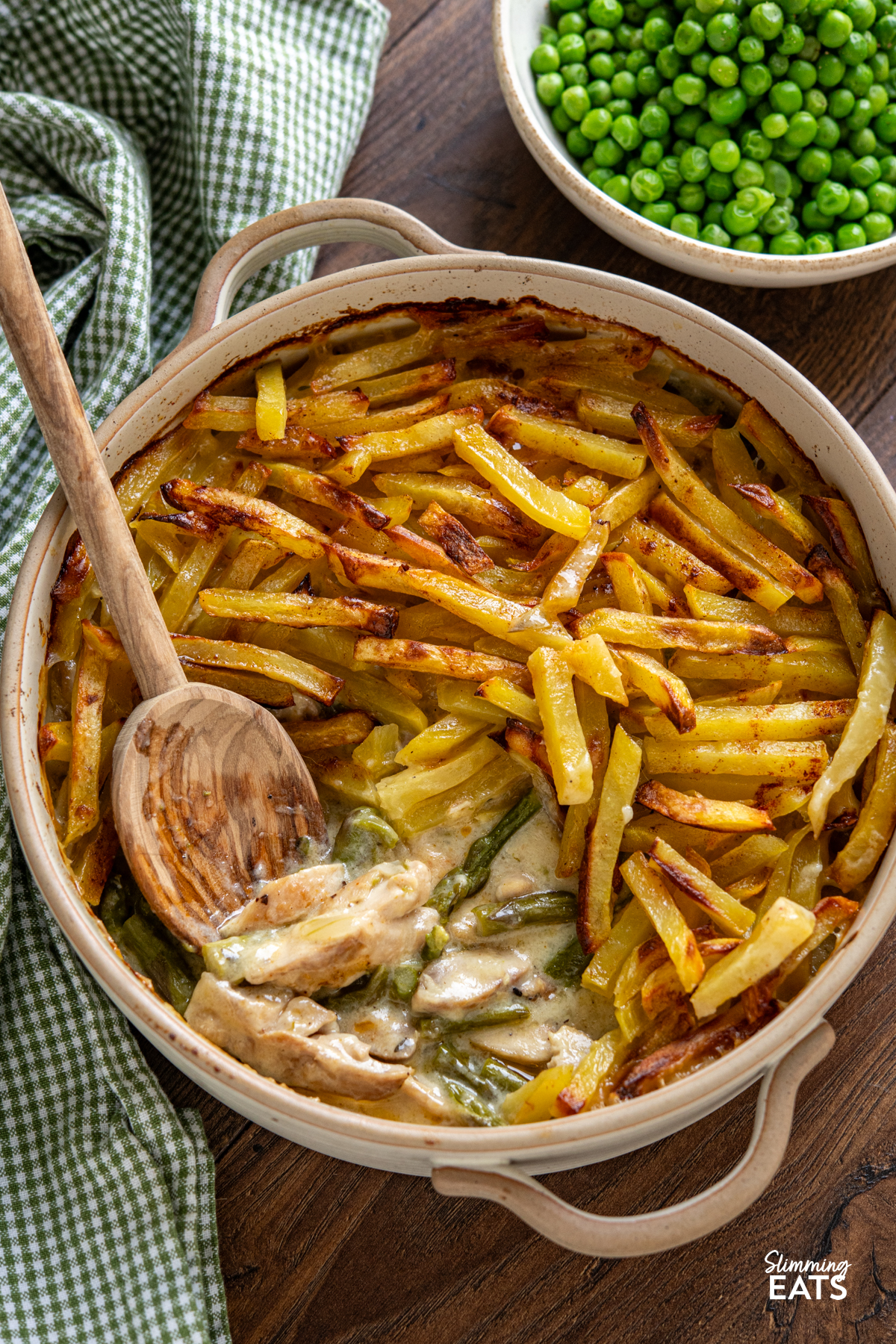 This Chicken and Asparagus Pie with Crispy Potatoes has a creamy, comforting filling topped with golden crispy potatoes for a delicious twist on a classic pie. Crispy Potato Topped Chicken and Asparagus Pie in ceramic oven dish with two handles surrounded by a bowl of garden peas