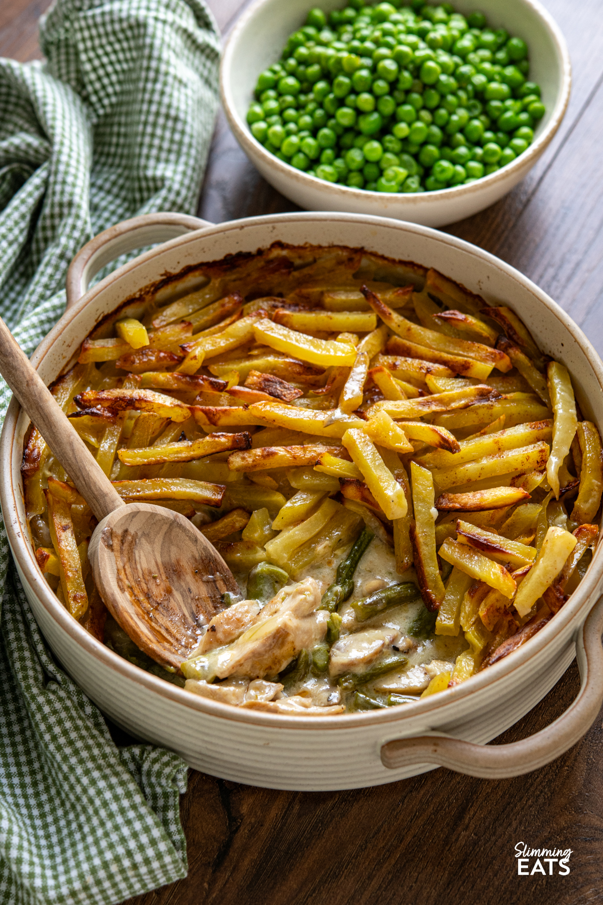 This Chicken and Asparagus Pie with Crispy Potatoes has a creamy, comforting filling topped with golden crispy potatoes for a delicious twist on a classic pie. Crispy Potato Topped Chicken and Asparagus Pie in ceramic oven dish with two handles surrounded by a bowl of garden peas