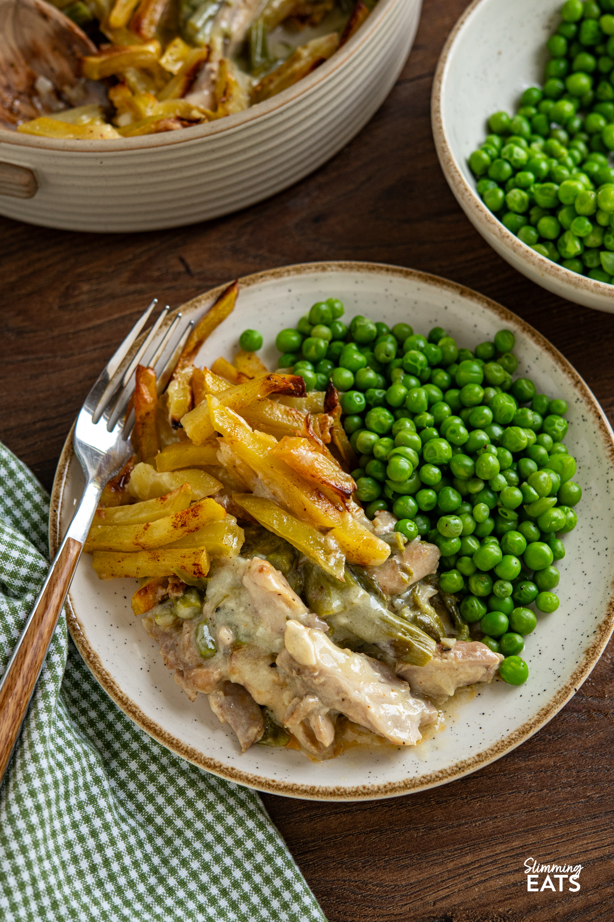 This Chicken and Asparagus Pie with Crispy Potatoes has a creamy, comforting filling topped with golden crispy potatoes for a delicious twist on a classic pie. serving of Crispy Potato Topped Chicken and Asparagus Pie on a white plate with beige rim, fork place on left