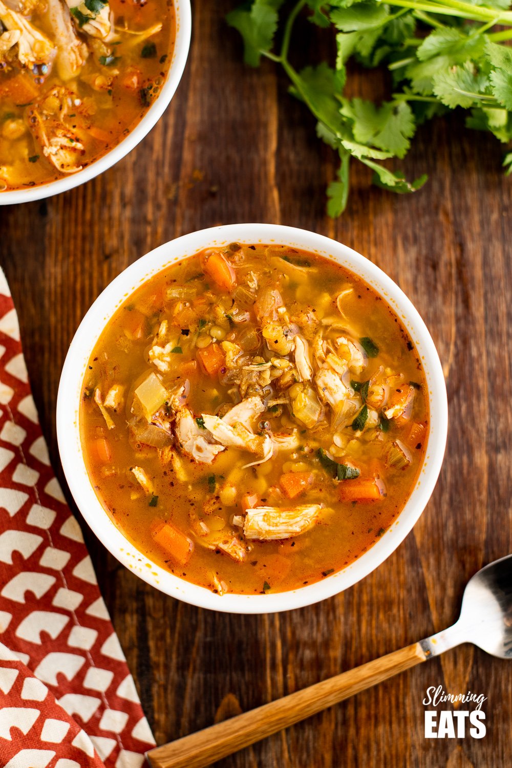 over the top view of chicken and lentil soup in white bowl on wooden board