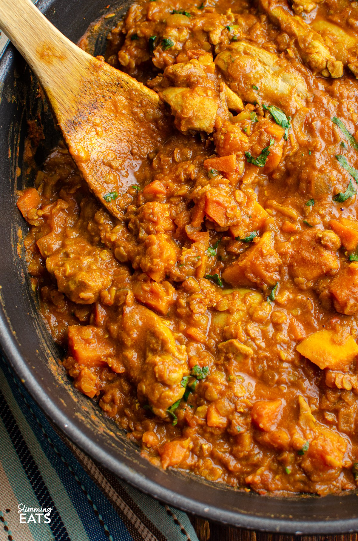 close up of Chicken, Sweet Potato and Lentil Curry in a black frying pan with wooden spoon.