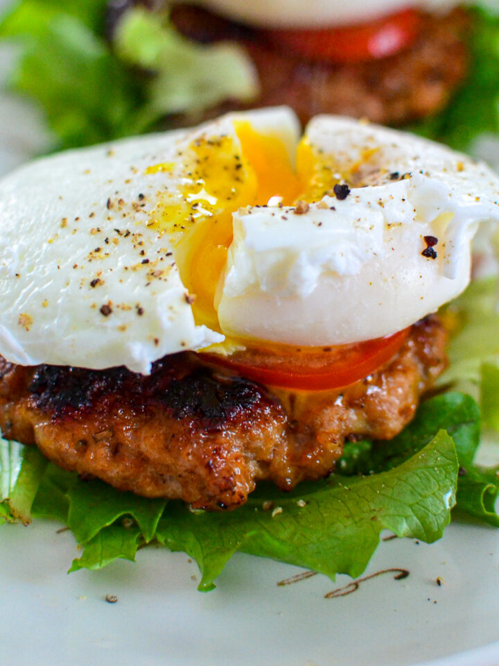 Homemade sausage patties over a bed of lettuce, topped with tomato and a poached egg, seasoned with salt and black pepper.
