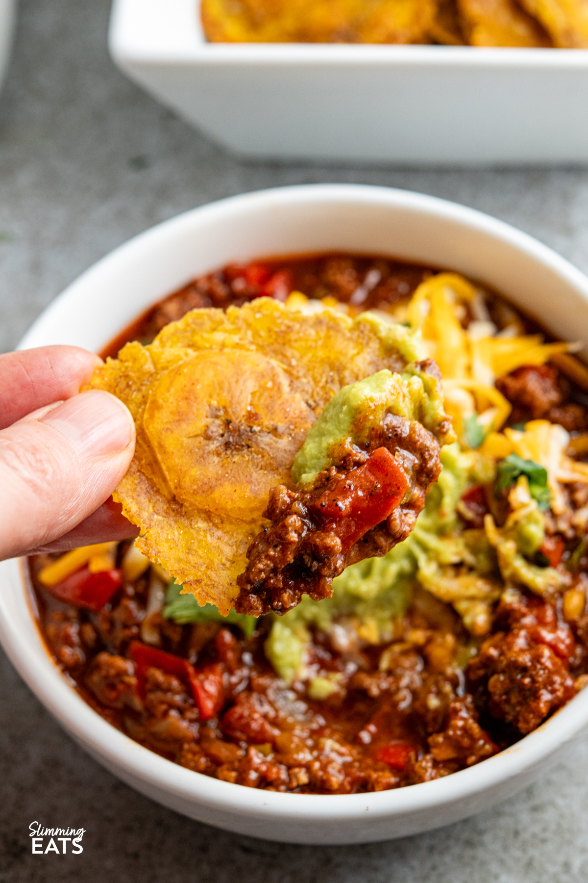 golden baked tostones scooping up some chilli form a bowl