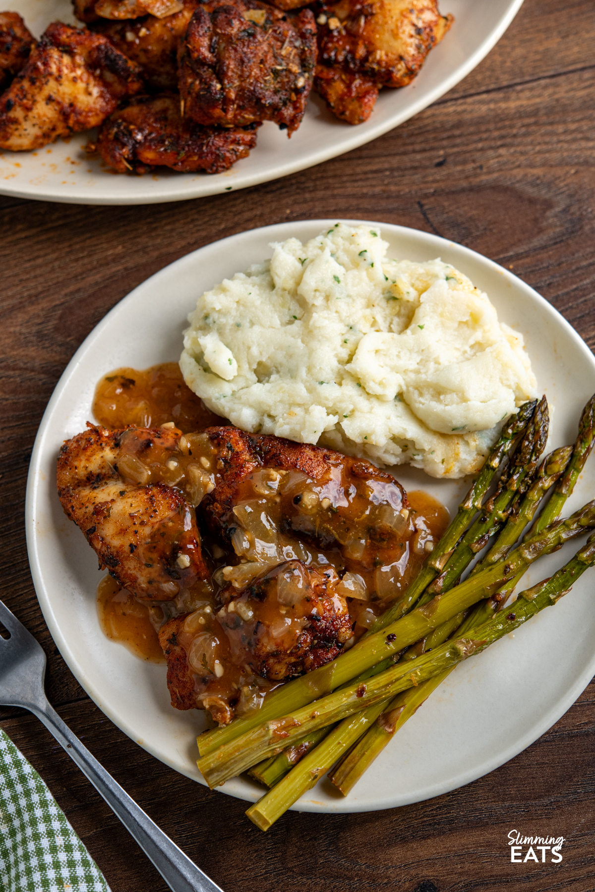 seasoned chicken and asparagus on a white plate with spring onion mash, sauce poured over chicken