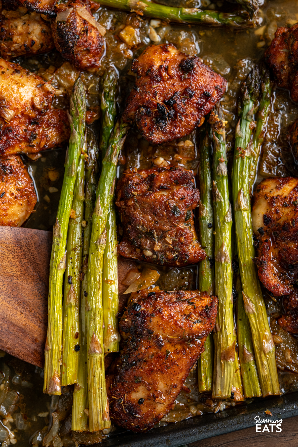 close up of seasoned chicken, asparagus with sauce on a sheet pan