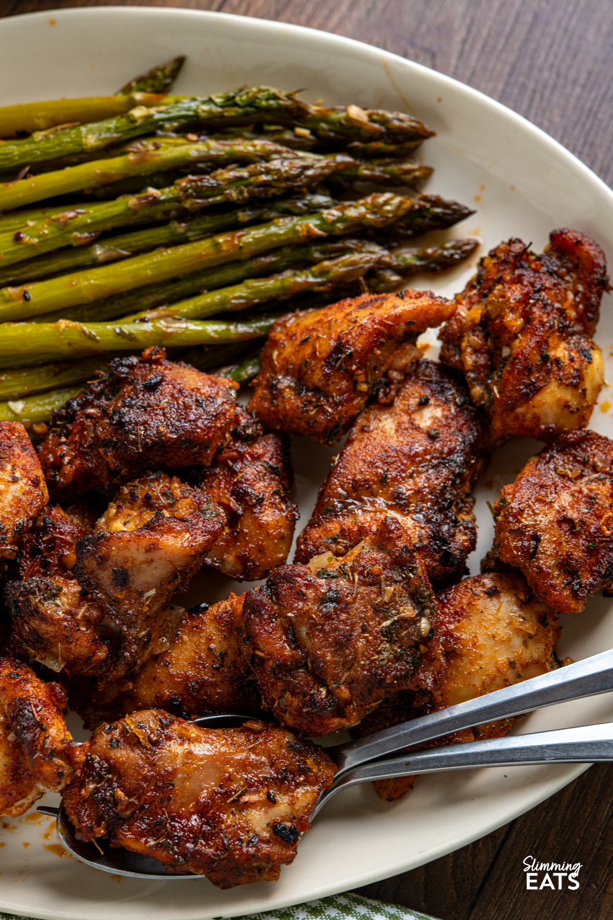 seasoned chicken, asparagus on a oval plate with spoon and fork, then jug with the sauce next to plate with spring onion mash