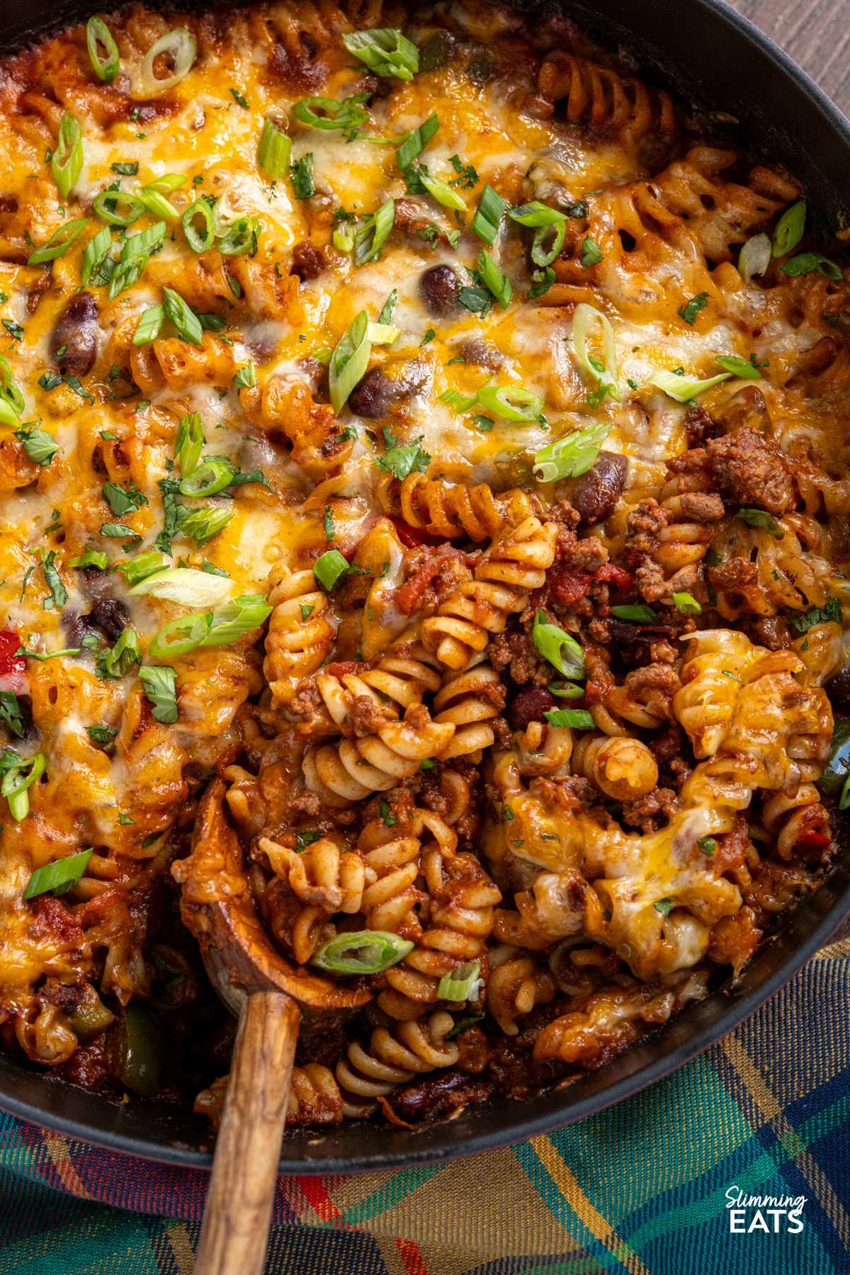 Mexican pasta bake is a hearty, comforting family meal that combines a rich beef chilli with pasta and a golden cheesy topping. close up of Mexican pasta bake in a staub cherry cast iron double handled pan