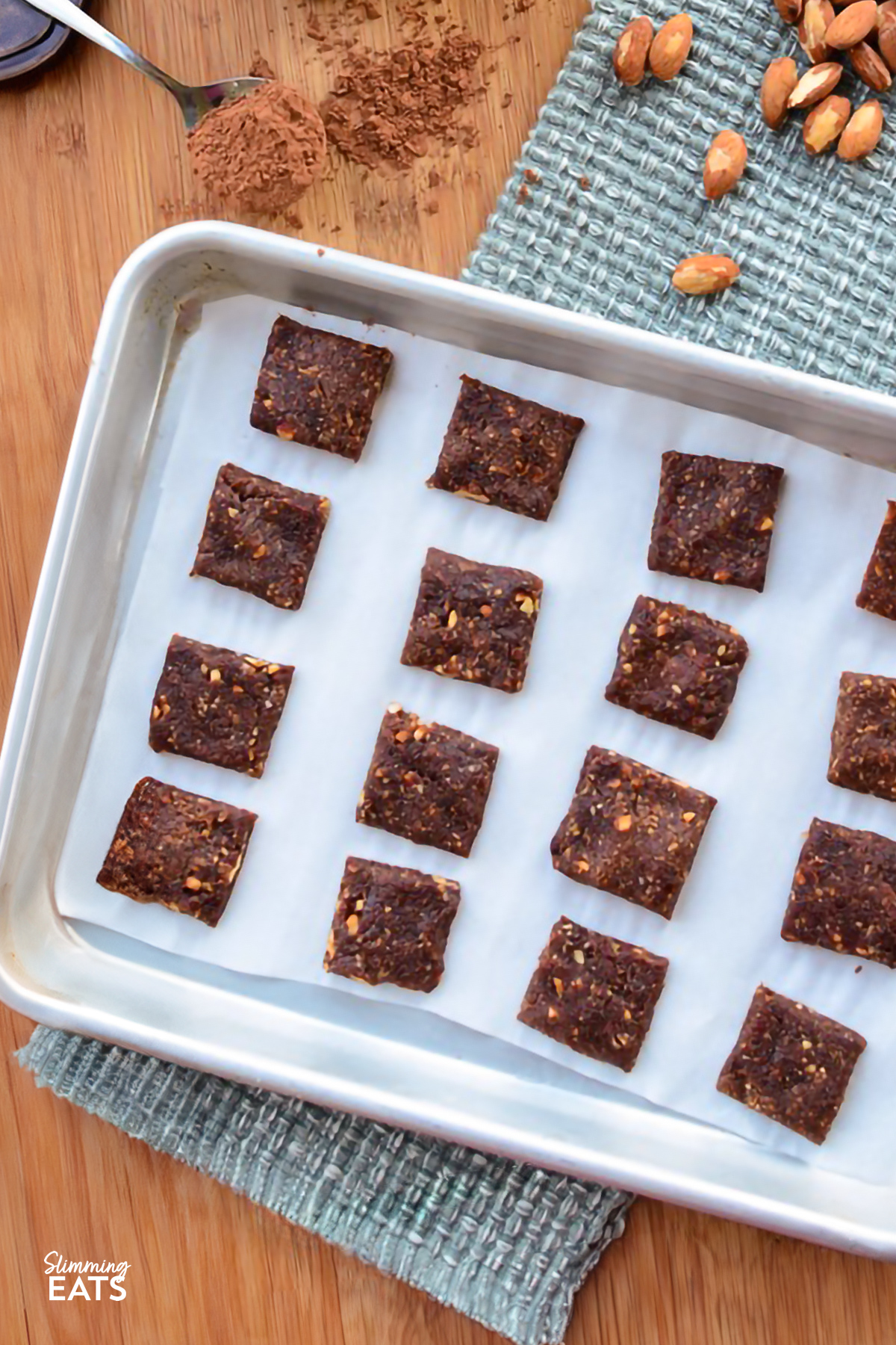 Healthy Chocolate Orange Bites on a parchment lined tray with scattered almonds and cocoa powder on a spoon