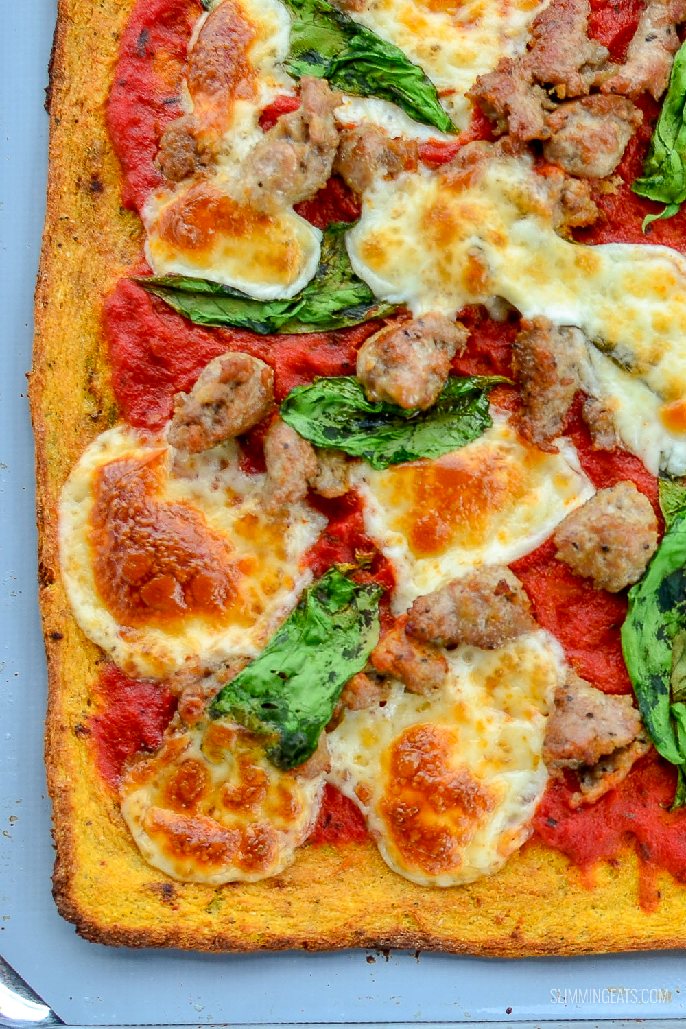 cauliflower pizza on baking tray with sausage and spinach