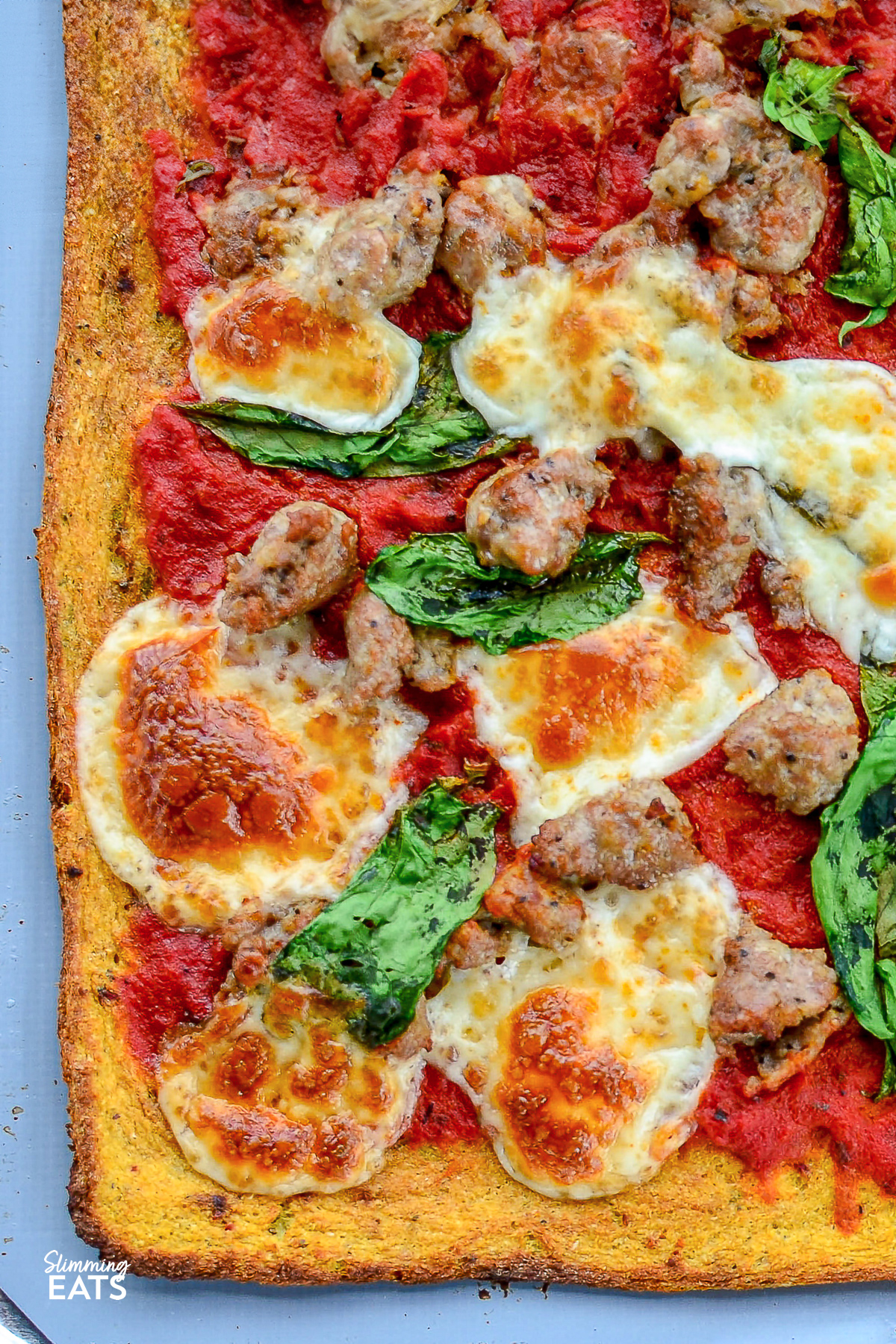 cauliflower pizza topped with mozzarella, sausage and spinach on a baking tray. 