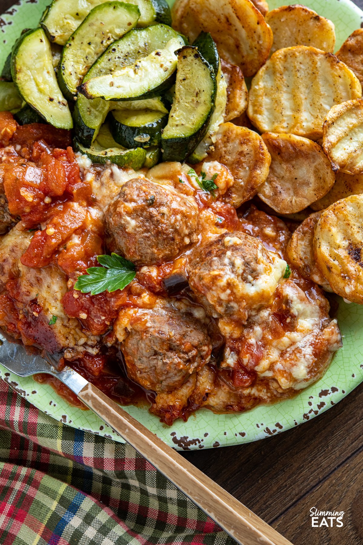 Indulge in the tantalizing flavors of the Mediterranean with this delicious creation of Moussaka Meatballs - tender seasoned lamb meatballs in a rich tomato sauce topped with a light creamy Bechamel sauce. Get ready to embark on a culinary journey that will transport your taste buds straight to the sun-soaked shores of Greece! close up of moussaka meatballs on light green plate with crispy potato slices and courgette