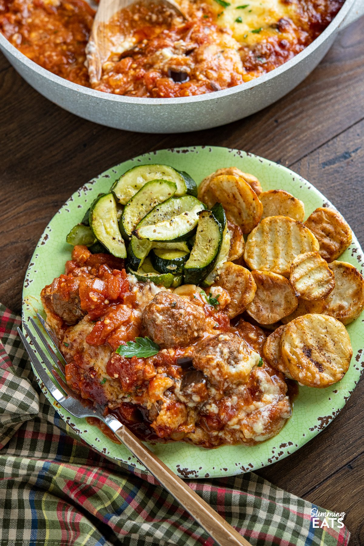 Indulge in the tantalizing flavors of the Mediterranean with this delicious creation of Moussaka Meatballs - tender seasoned lamb meatballs in a rich tomato sauce topped with a light creamy Bechamel sauce. Get ready to embark on a culinary journey that will transport your taste buds straight to the sun-soaked shores of Greece! moussaka meatballs on light green plate with crispy potato slices and courgette