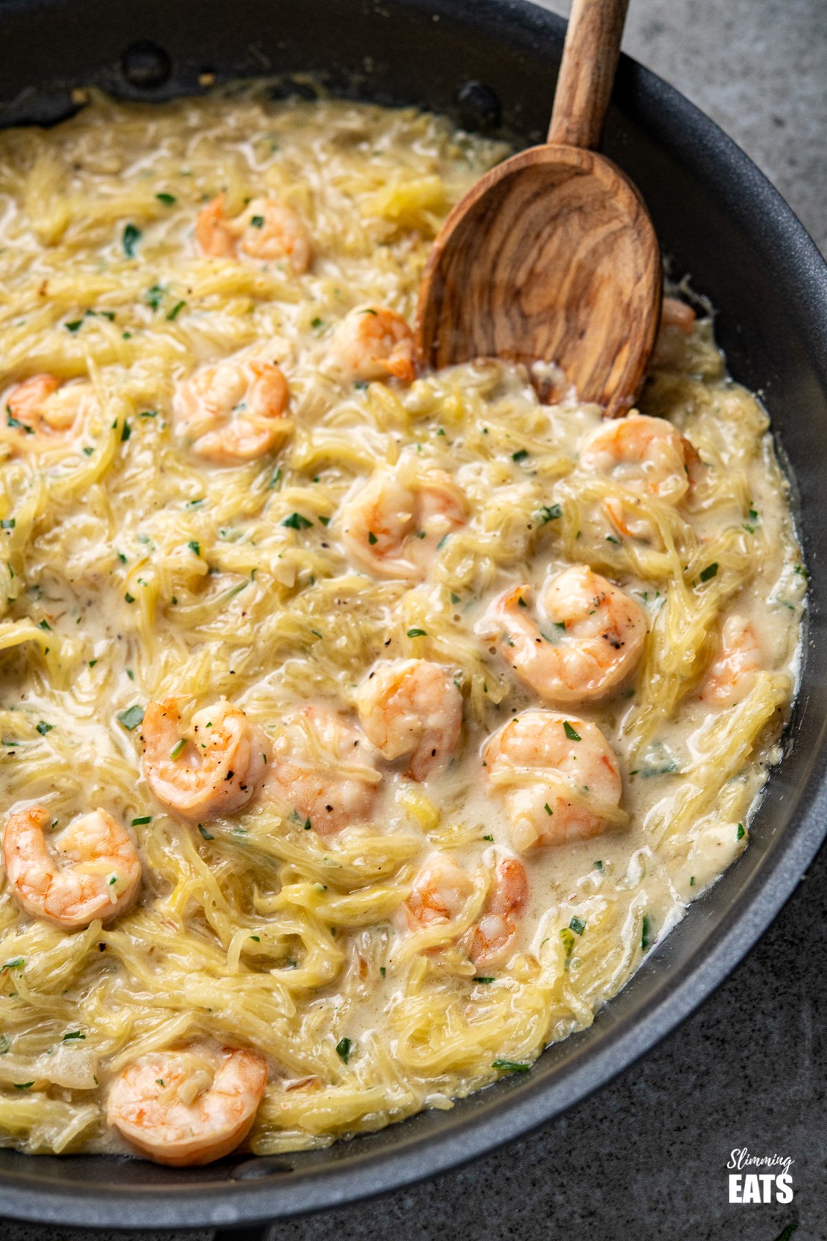 Shrimp Spaghetti Squash Alfredo - delicious shrimp in a creamy dairy free Alfredo sauce with low carb spaghetti squash. A perfect pasta alternative dish. #dairyfree #lowcarb #slimmingworld #weightwatchers close up of Shrimp Spaghetti Squash Alfredo in a black frying pan with olive wood spoon