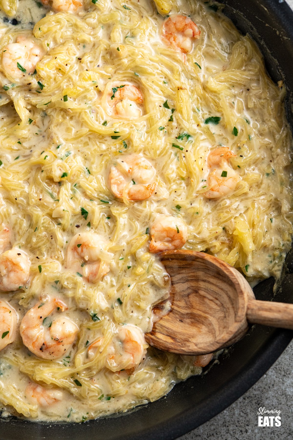 Shrimp Spaghetti Squash Alfredo - delicious shrimp in a creamy dairy free Alfredo sauce with low carb spaghetti squash. A perfect pasta alternative dish. #dairyfree #lowcarb #slimmingworld #weightwatchers close up of Shrimp Spaghetti Squash Alfredo in a black frying pan with olive wood spoon