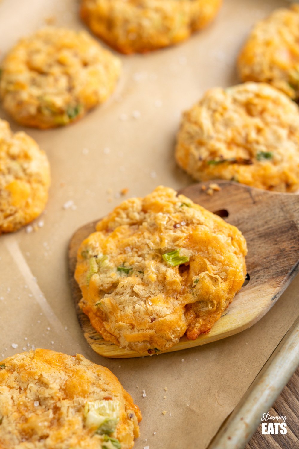 close up of cheddar butter bean bites on wooden spatula from parchment paper lined baking tray