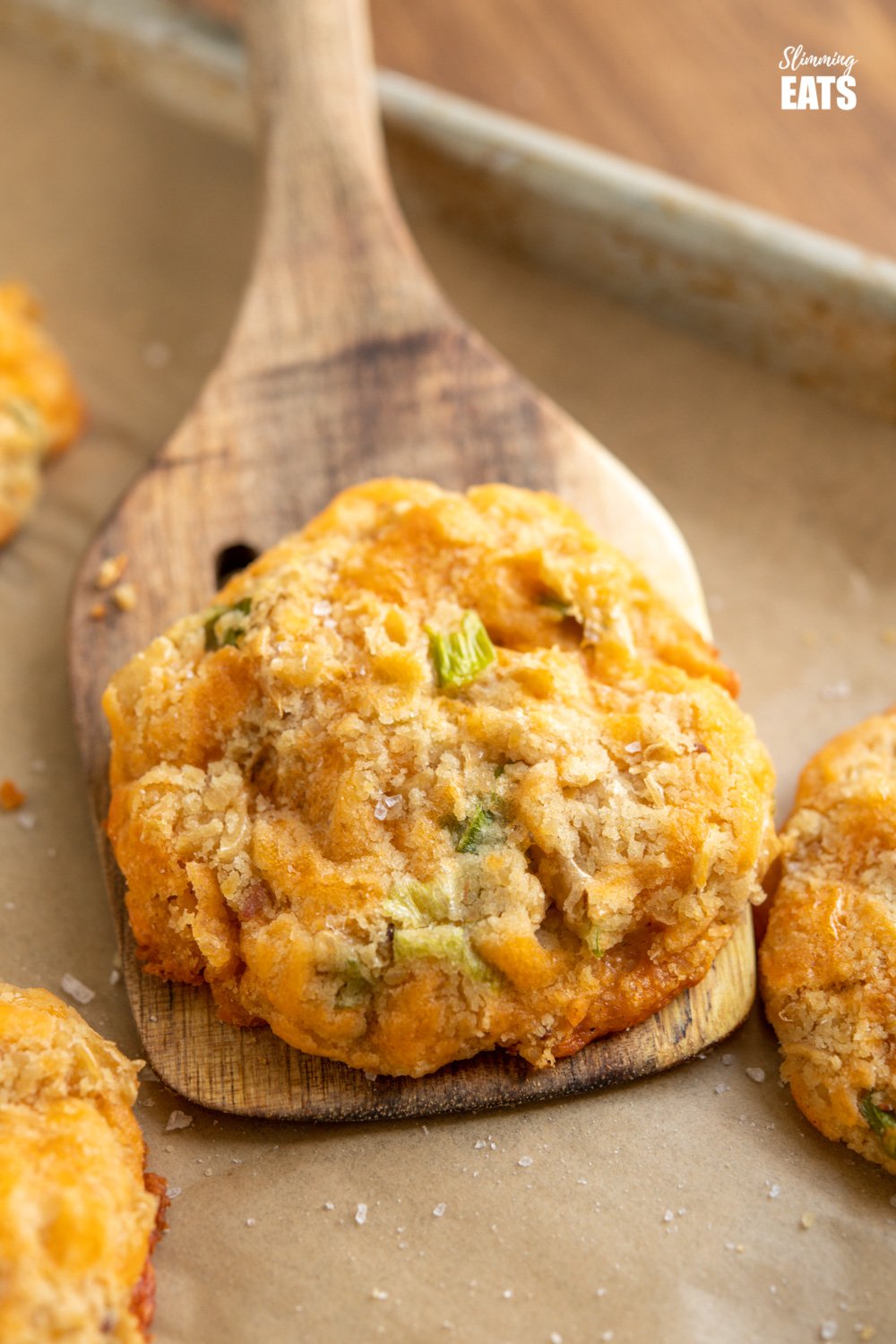 close up of cheddar butter bean bites on wooden spatula from parchment paper lined baking tray