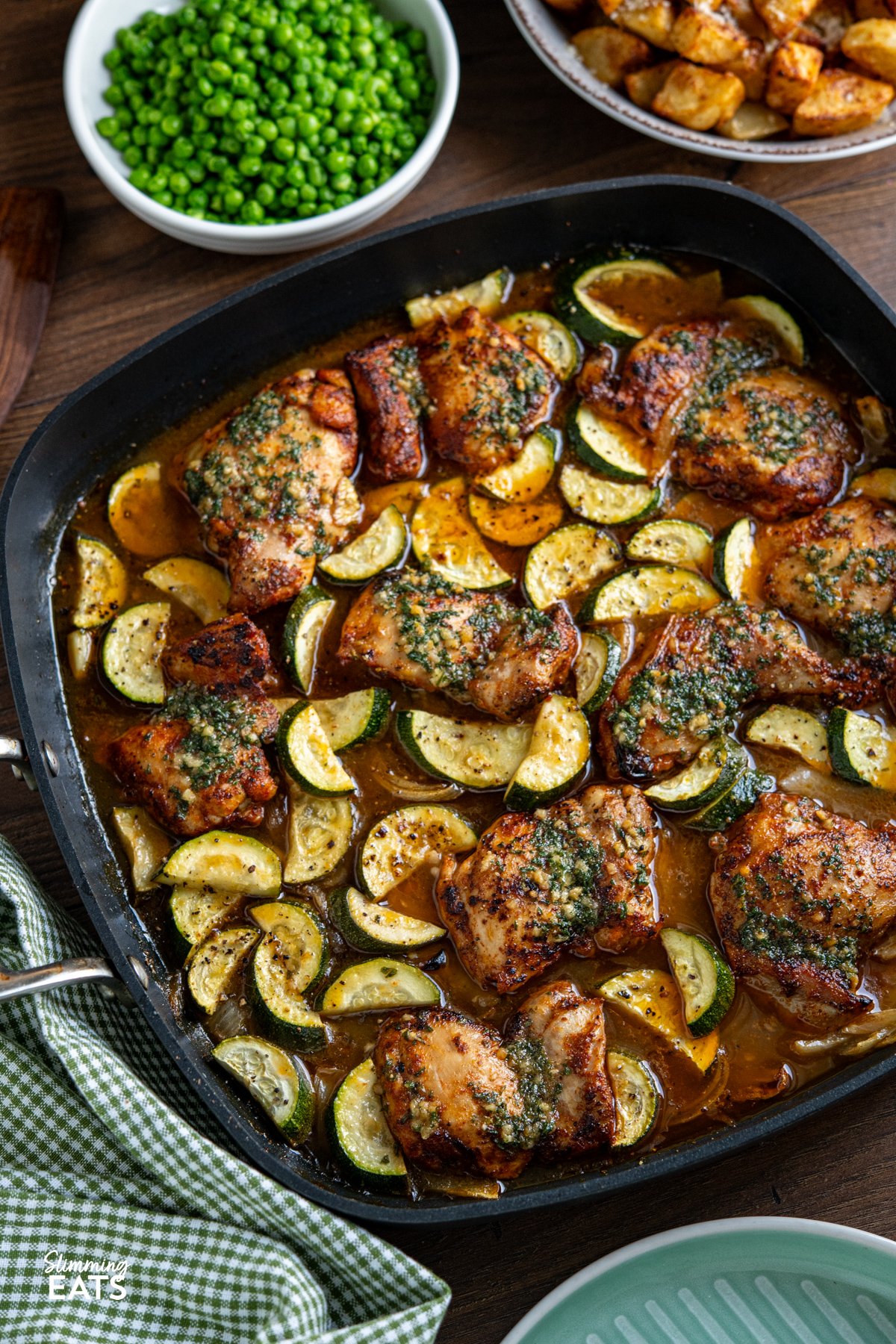 This Lemon Garlic Chicken and Zucchini Bake is an easy, delicious meal. Juicy chicken is nestled in a zesty lemon and garlic butter sauce with tender seasoned zucchini. Garlic Lemon Chicken and Zucchini Bake in a all-clad square skillet with bowl of peas and golden potatoes in background
