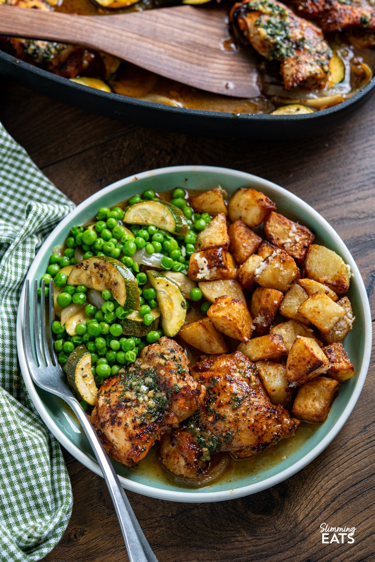 This Lemon Garlic Chicken and Zucchini Bake is an easy, delicious meal. Juicy chicken is nestled in a zesty lemon and garlic butter sauce with tender seasoned zucchini. Garlic Lemon Chicken and Zucchini Bake served on a turquoise plate alongside golden parmesan potatoes and garden peas, with the skillet of baked chicken visible in the background.