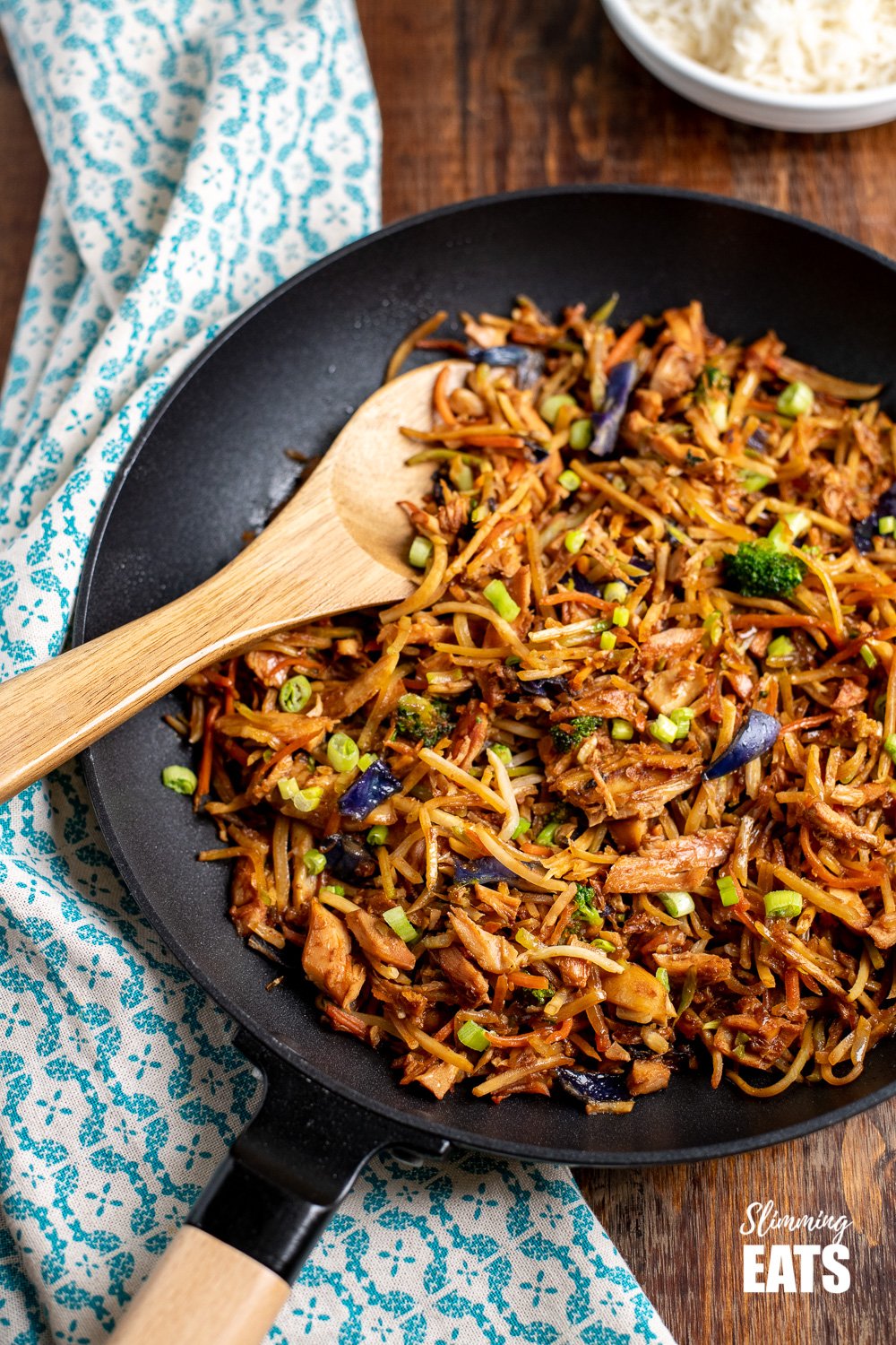 orange and ginger turkey stir fry in a black frying pan with wooden spoon