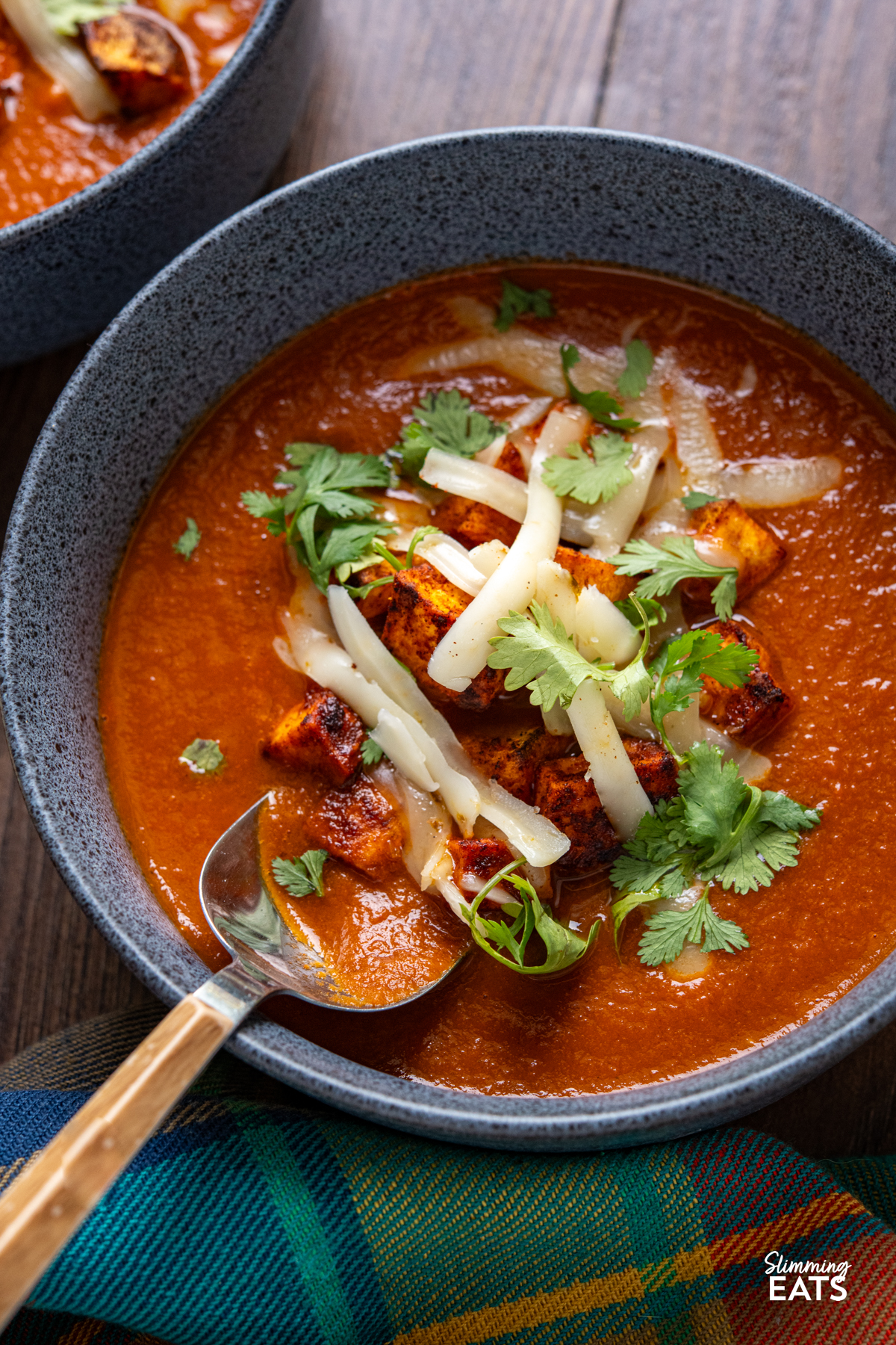 close up of spicy eggplant tomato soup in navy blue bowls topped with roasted sweet potato, cheddar and coriander.