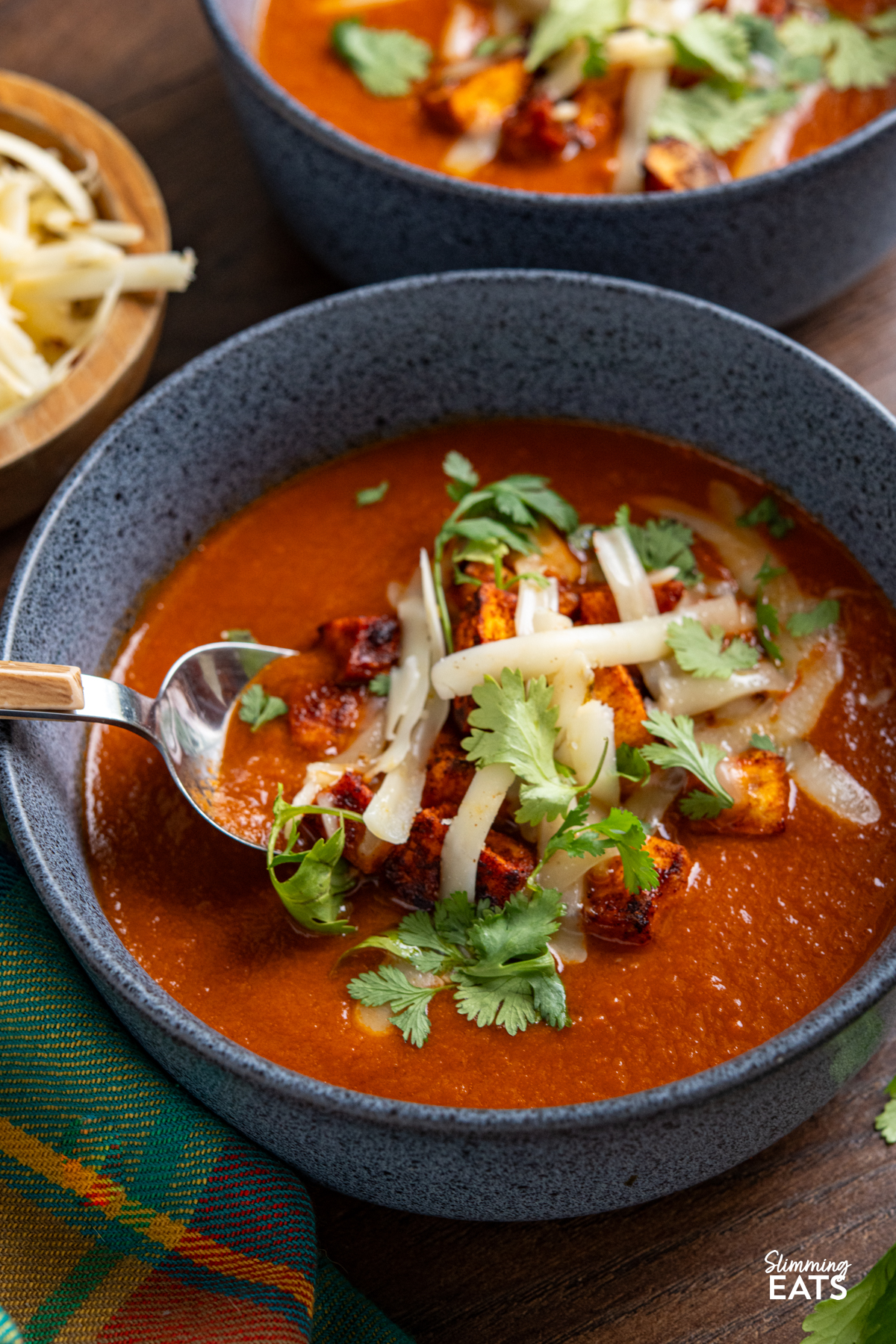 spicy eggplant tomato soup in navy blue bowls topped with roasted sweet potato, cheddar and coriander.