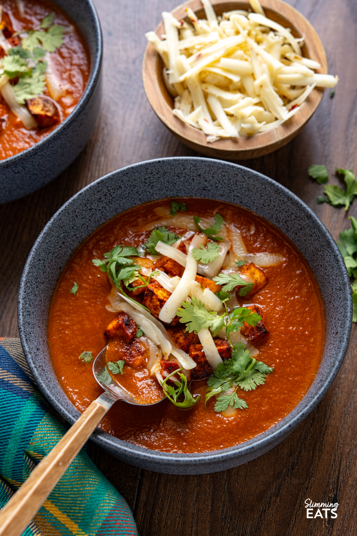 spicy eggplant tomato soup in navy blue bowls topped with roasted sweet potato, cheddar and coriander.