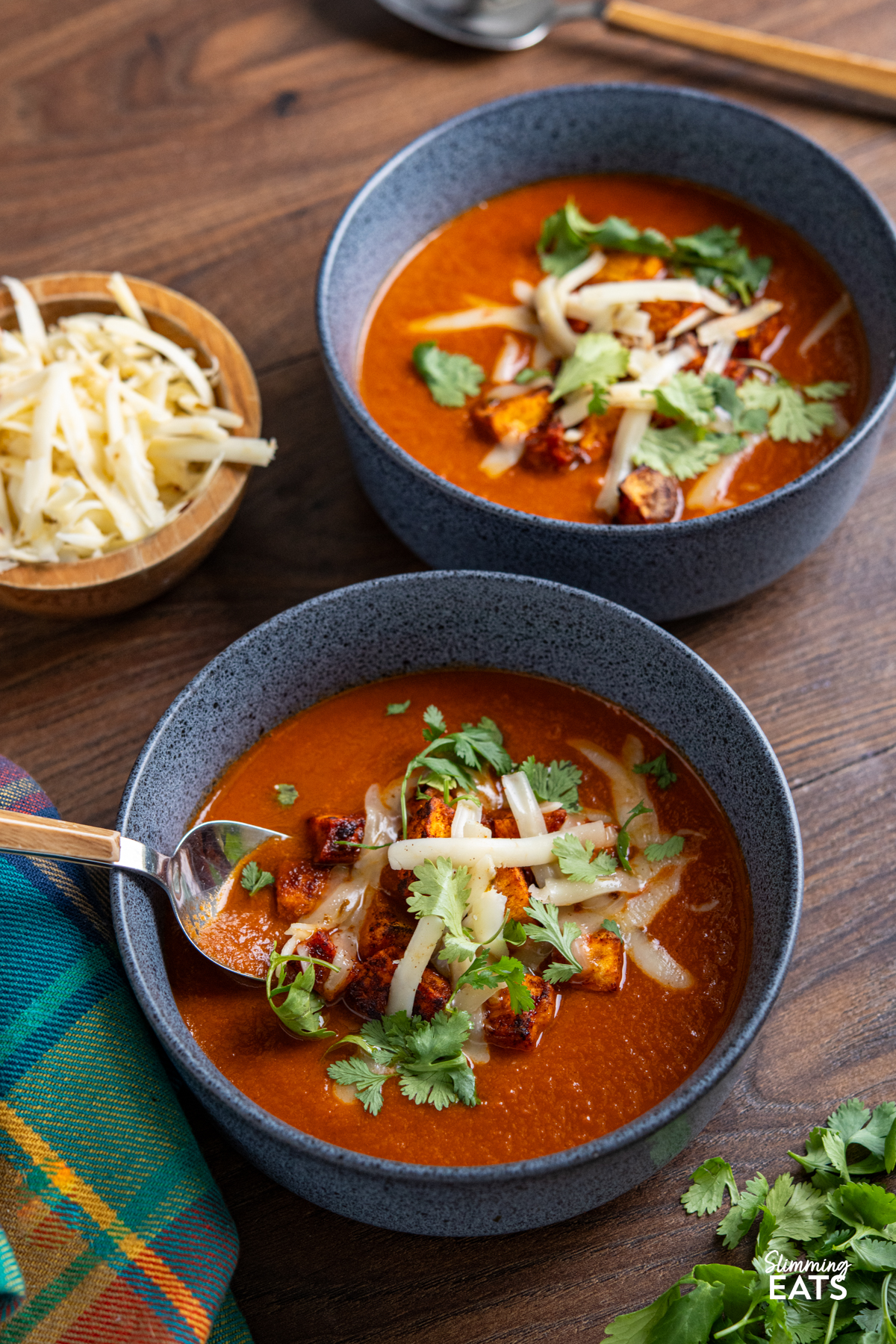 spicy eggplant tomato soup in navy blue bowls topped with roasted sweet potato, cheddar and coriander.