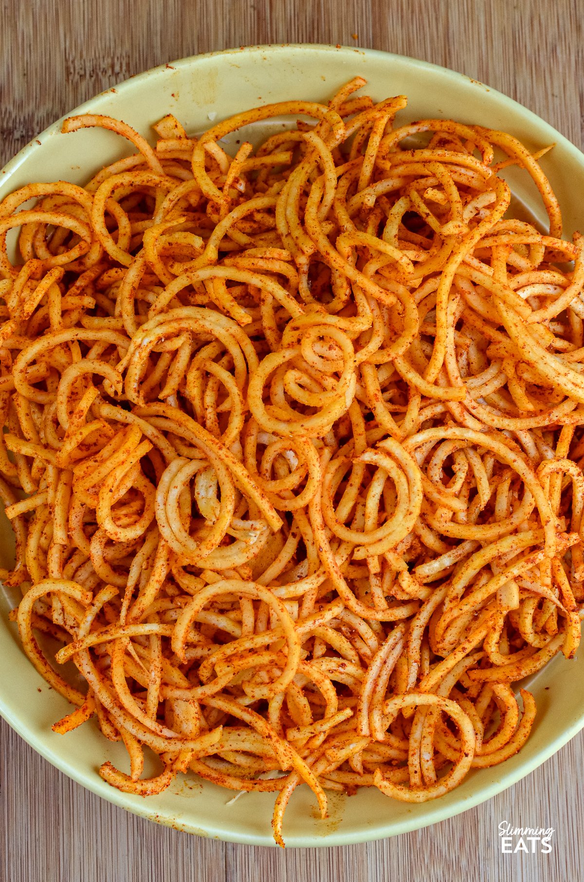 Spiralized Seasoned Swede Fries - these delightful spirals of swede offer a nutritious twist to traditional fries, ideal for those seeking a lower-carb alternative to accompany their high-protein main course. seasoned spiralized swede fries in a yellow bowl