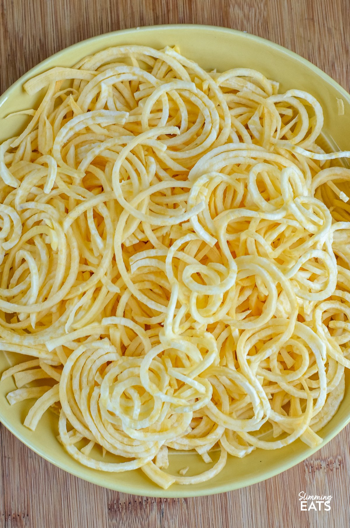 Spiralized Seasoned Swede Fries - these delightful spirals of swede offer a nutritious twist to traditional fries, ideal for those seeking a lower-carb alternative to accompany their high-protein main course. unseasoned spiralized swede fries in a yellow bowl