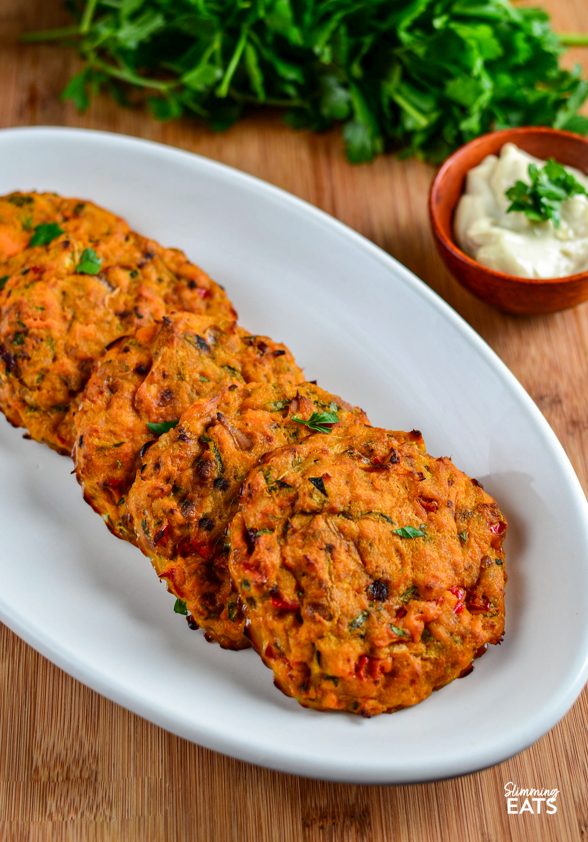 just baked Oven Baked Tuna Sweet Potato Patties on a white oval plate scattered with fresh parsley, small wooden bowl with mayo on the side
